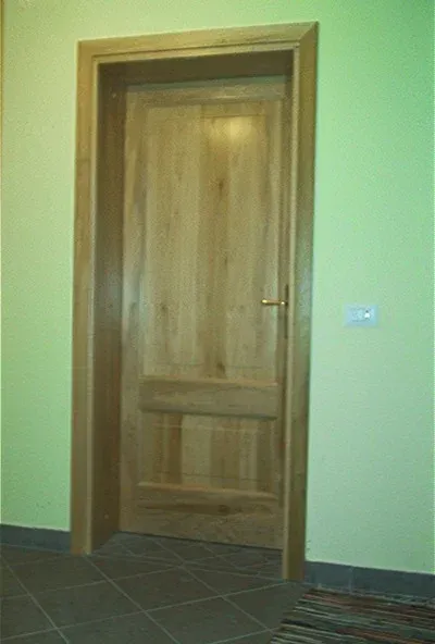 Porta e telaio in legno, incastonati in una parete verde chiaro. Pavimento piastrellato marrone.