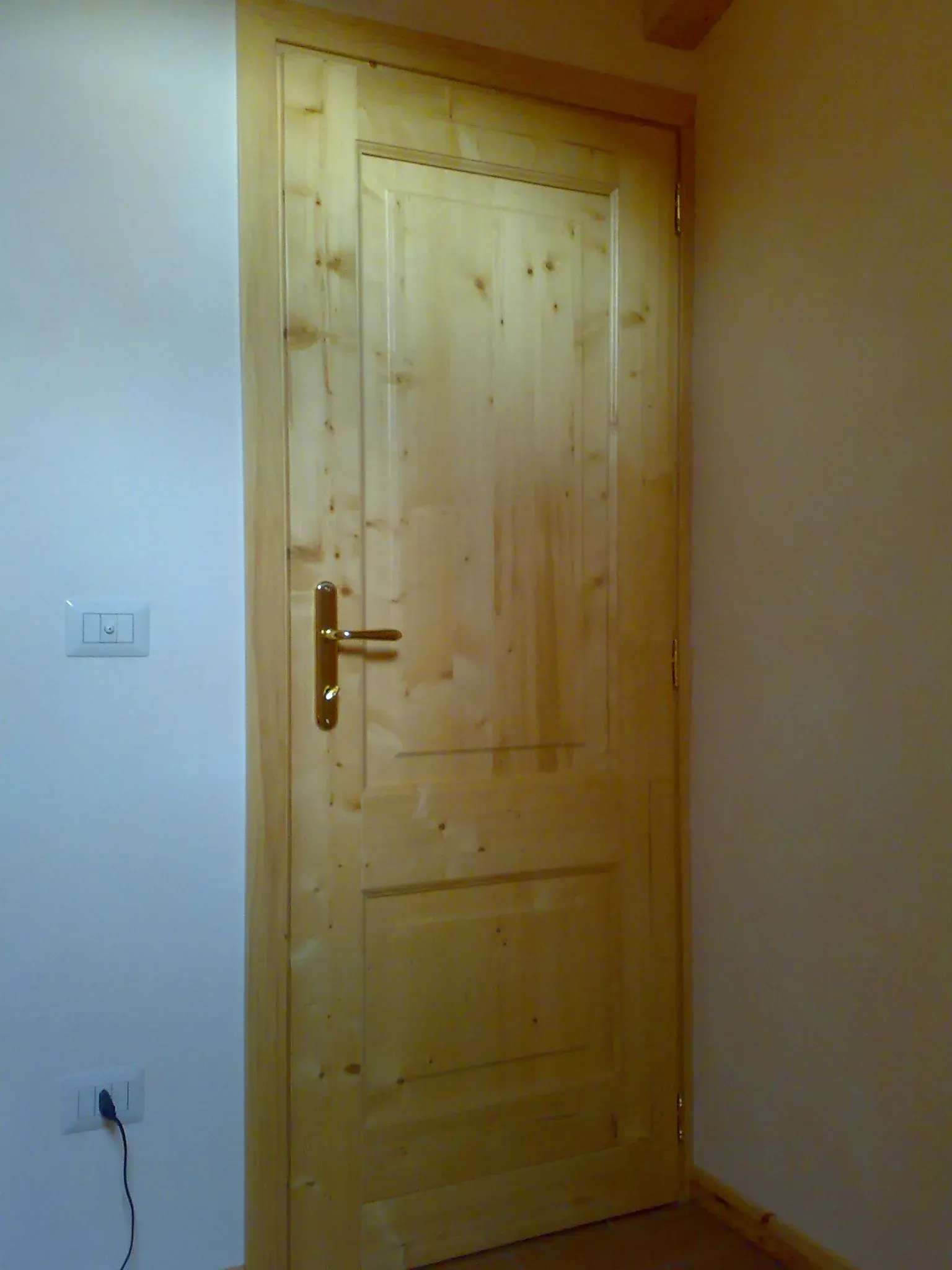 Porta in legno con maniglia in ottone, inserita in una parete di colore chiaro.