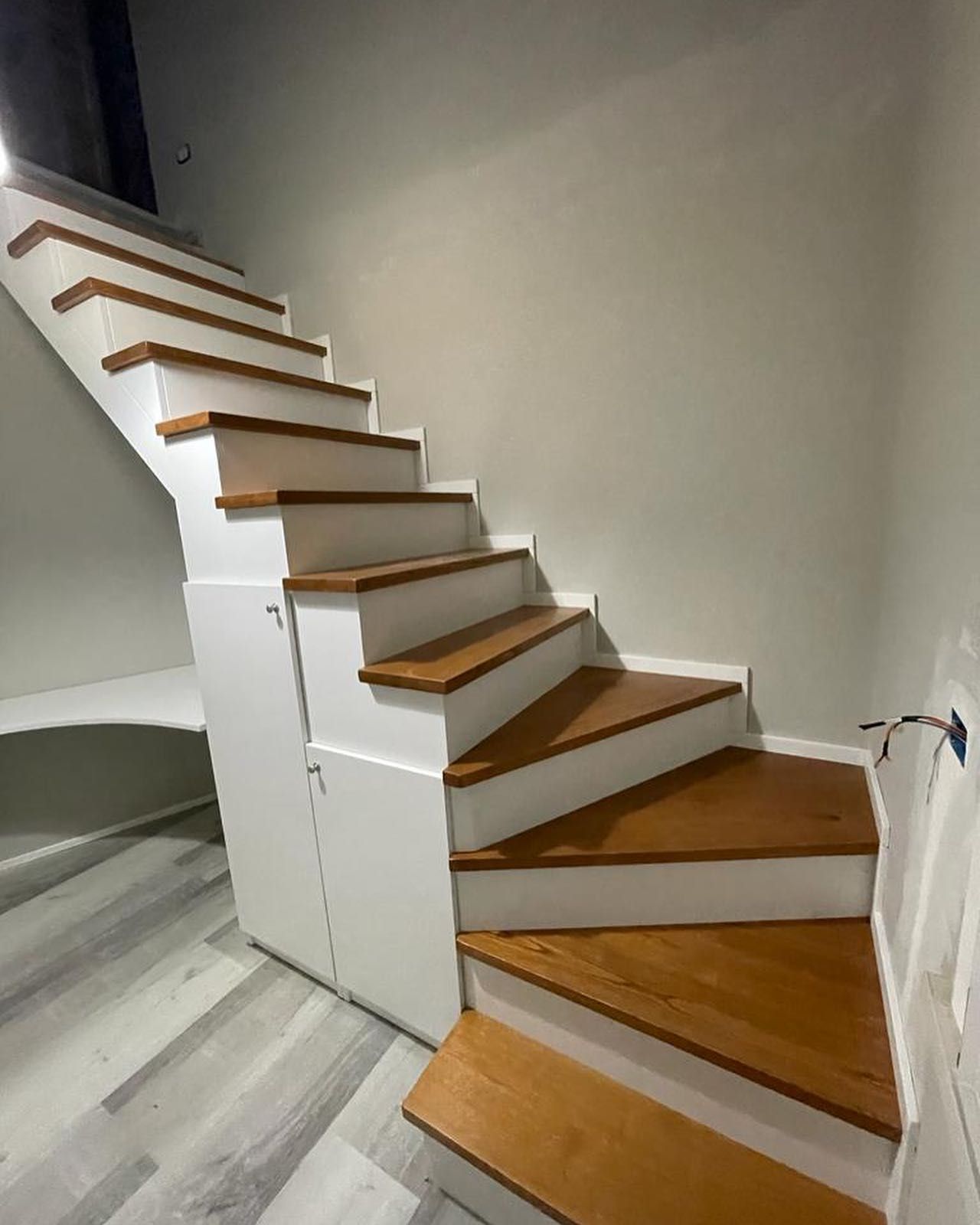 Scale in legno con alzate bianche e armadietti sottostanti.