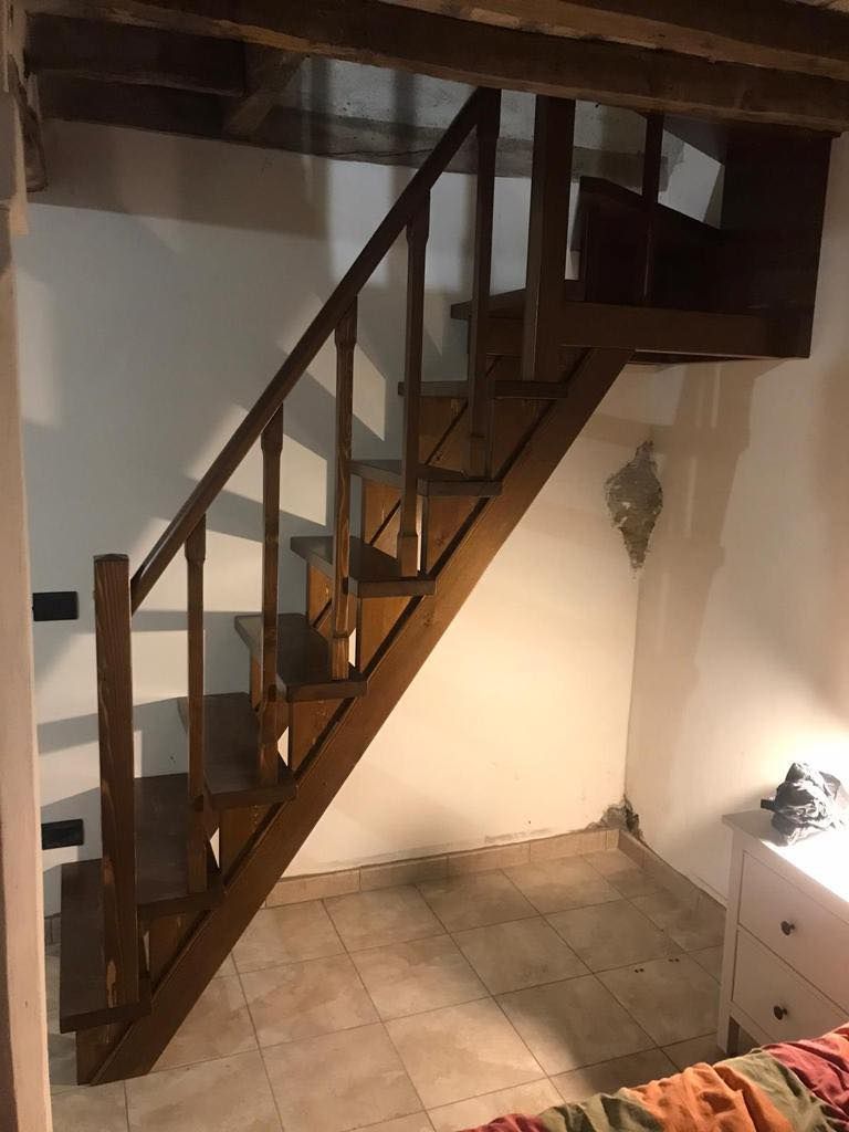 Scala in legno che conduce al piano superiore, con pareti bianche e pavimento piastrellato.