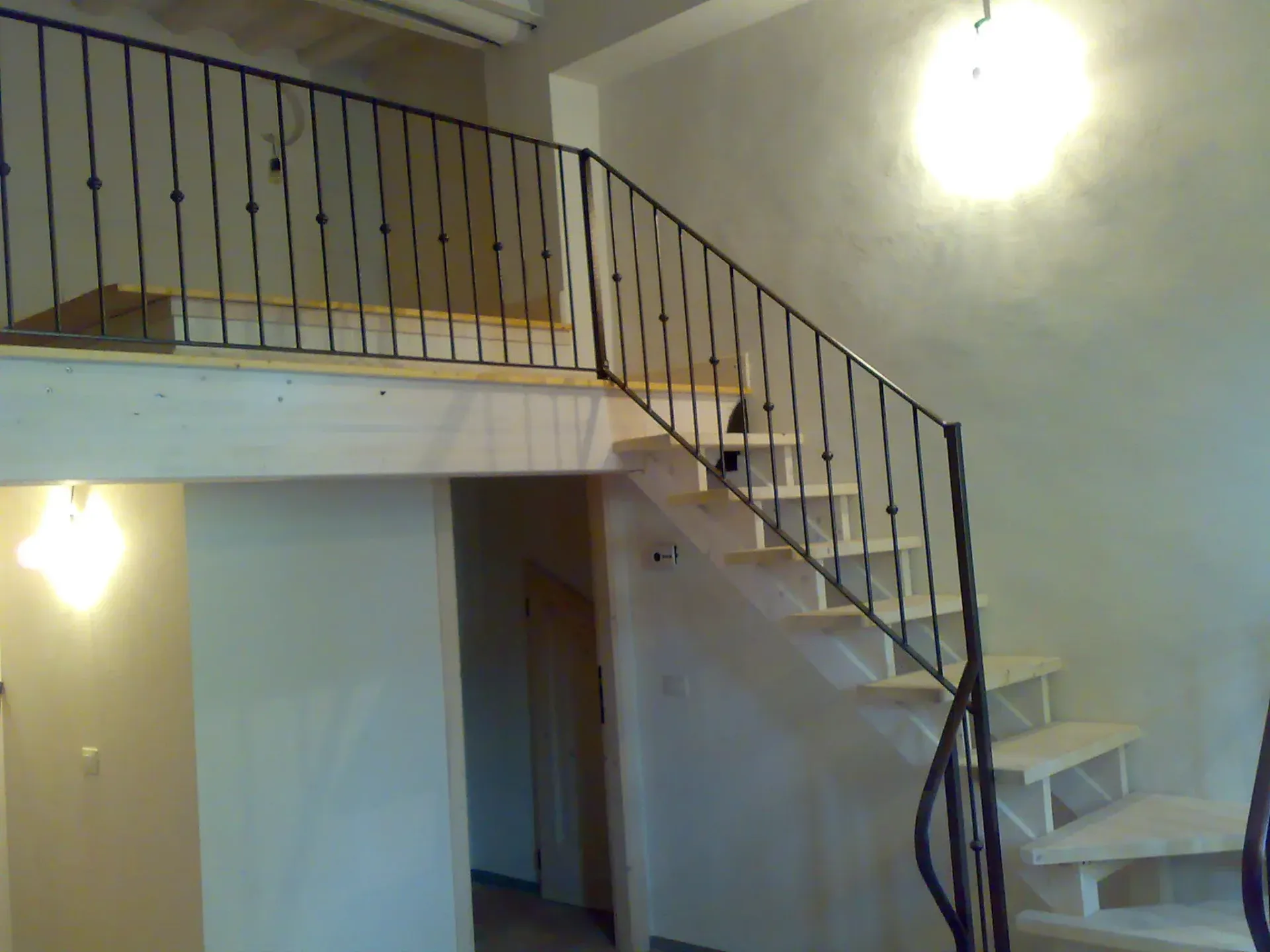 Interno con scala in legno e ringhiera in metallo nero che conduce a un soppalco.