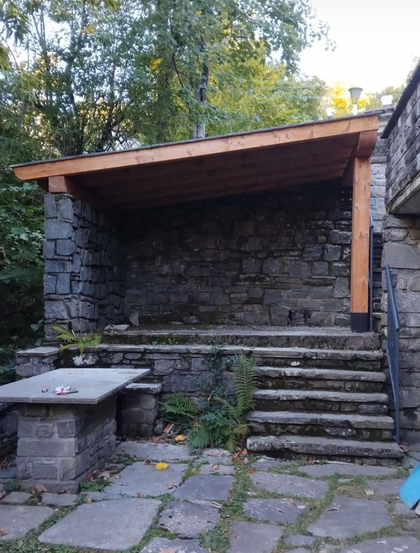 Patio in pietra con tettoia; gradini e tavolo in pietra, tetto in legno.
