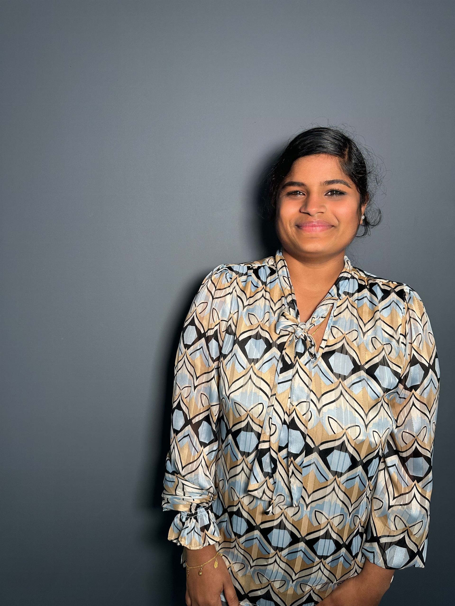 A woman in a snake print shirt is standing in front of a gray wall.