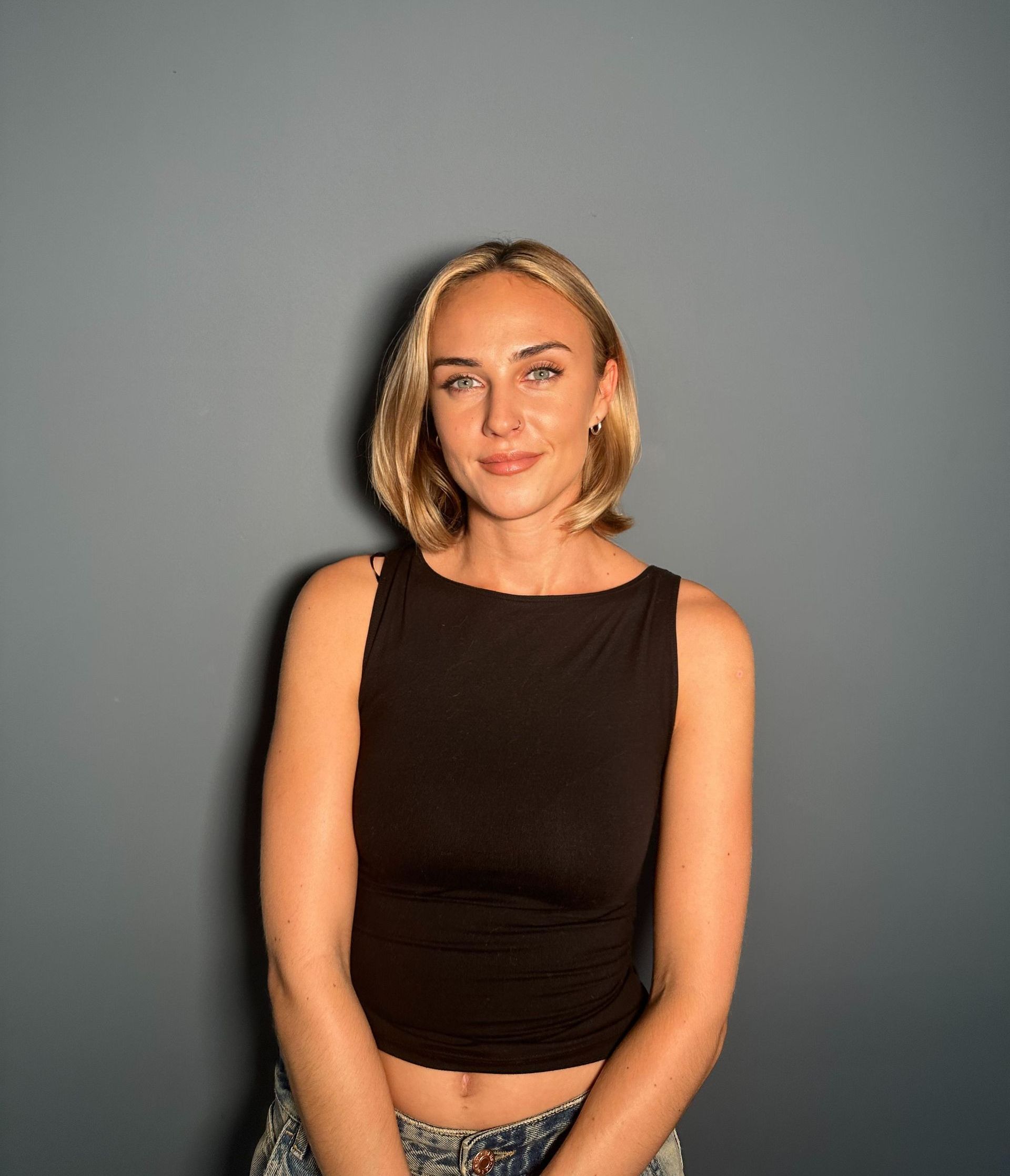 A woman in a black crop top is standing in front of a grey wall