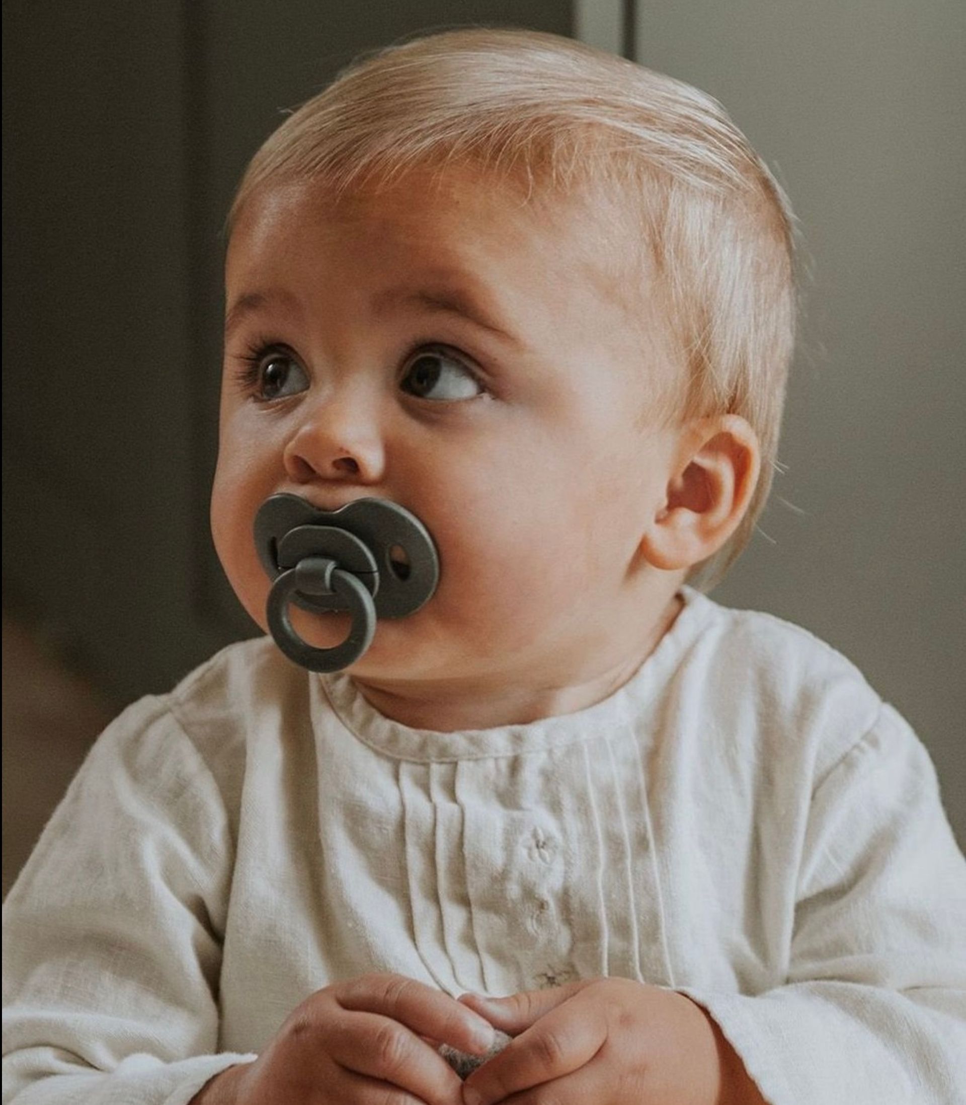 A baby with a pacifier in his mouth is wearing a white shirt.