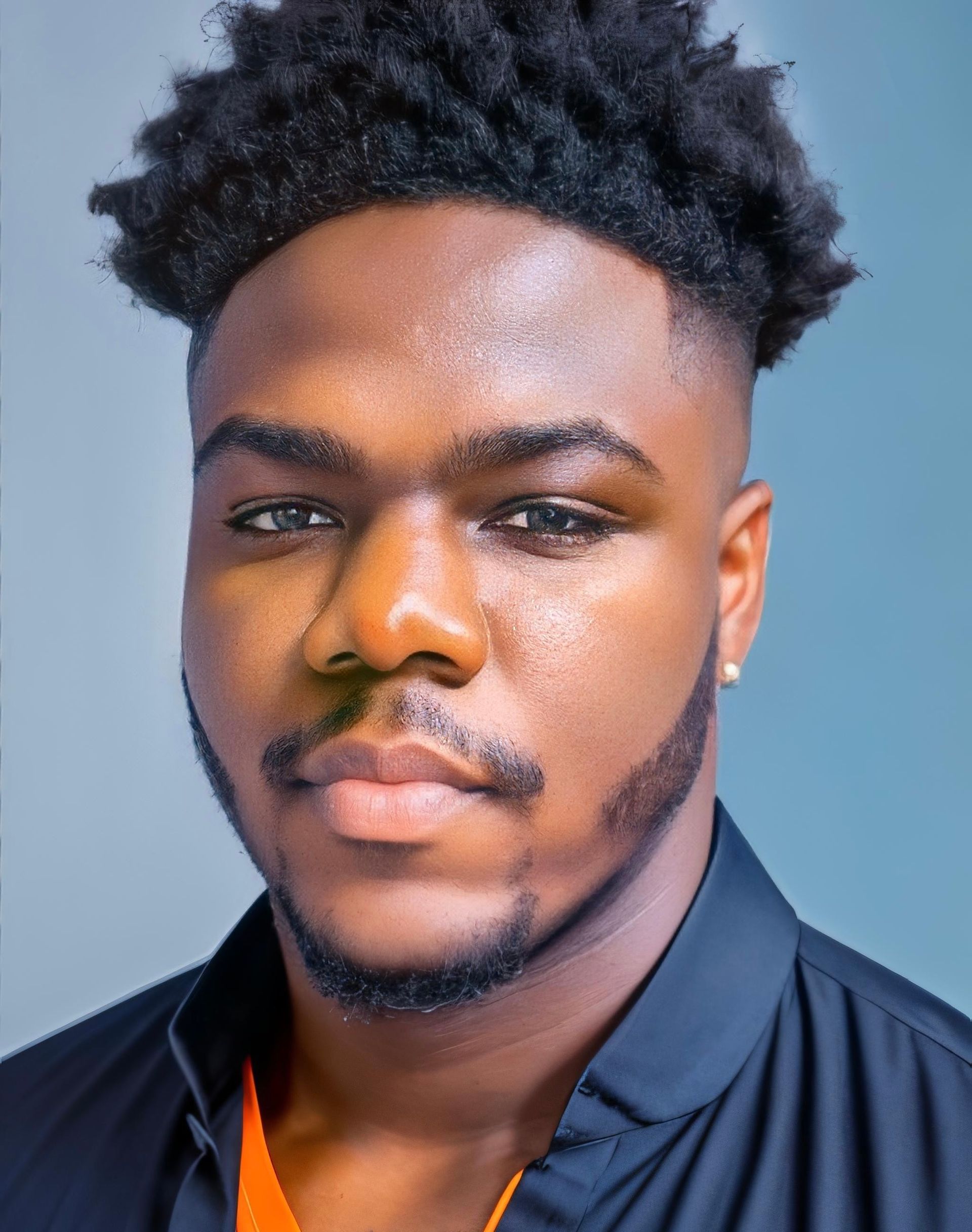 A young man with a beard and curly hair is looking at the camera.