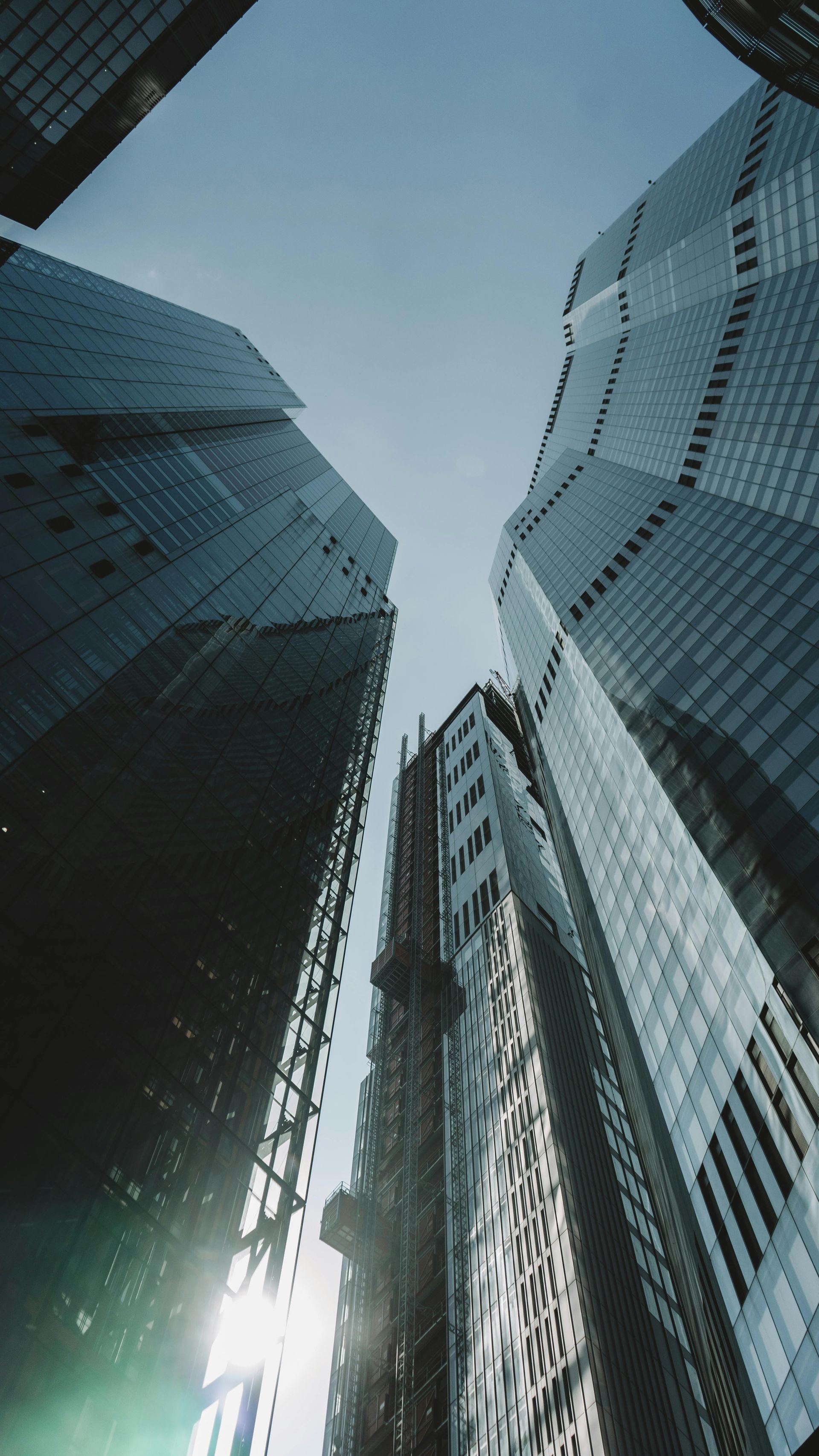 Skyscrapers from low angle, blue sky above. Sunlight gleams off glass facades.