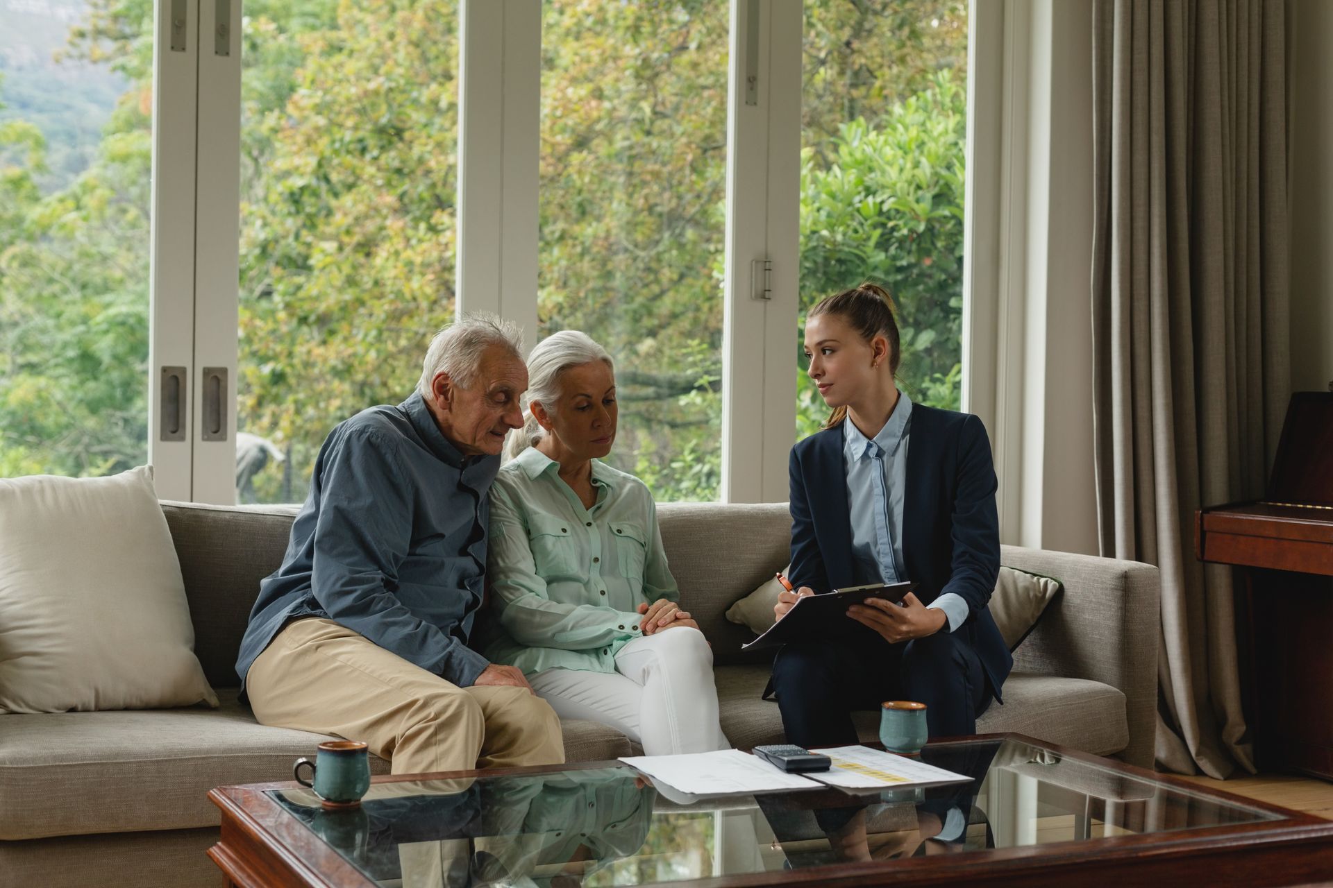 A financial advisor discusses documents with a couple seated on a sofa in a living room.
