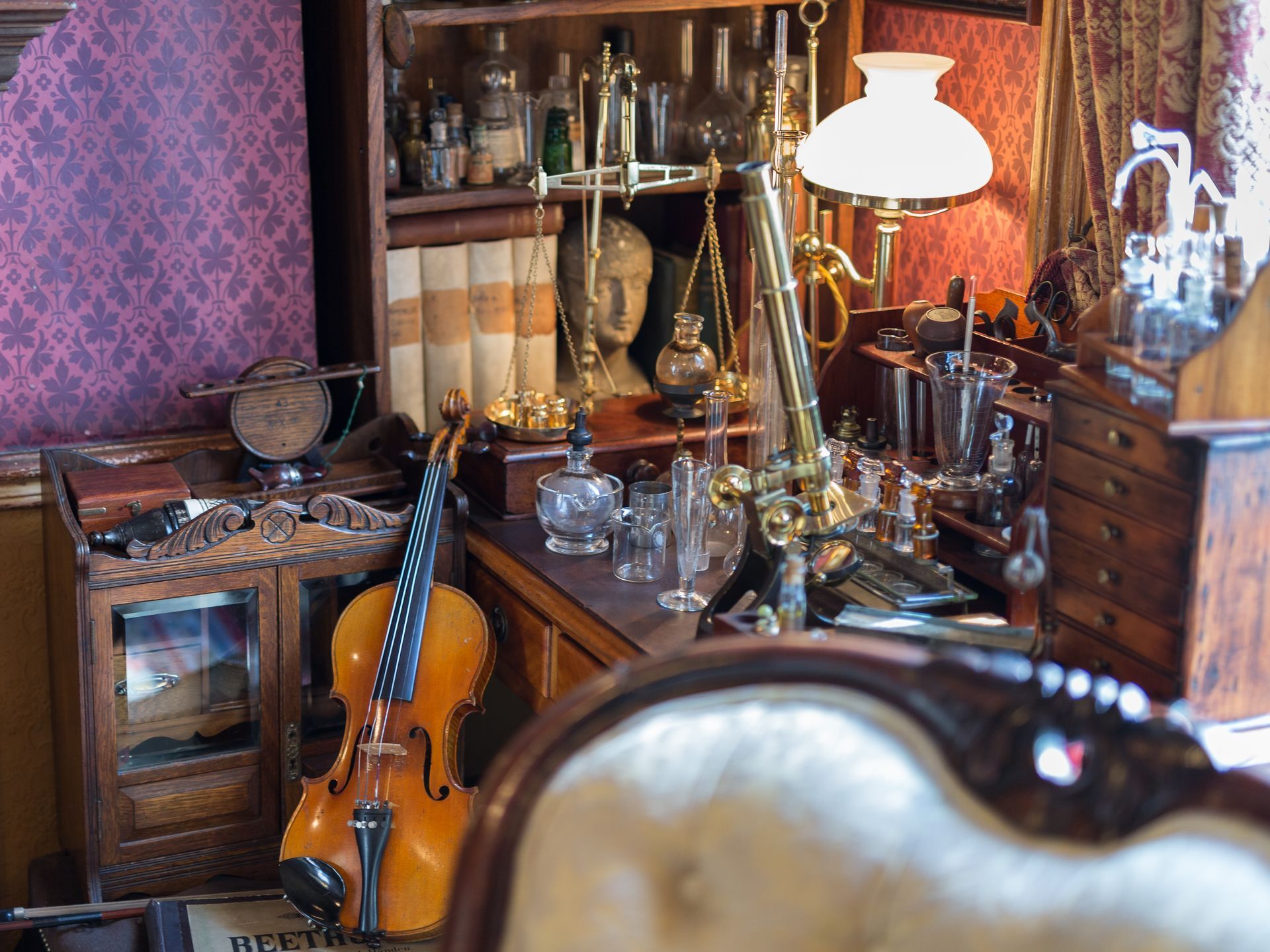 Detailed interior of a Victorian study with a violin, lamp, bookshelves, and scientific instruments.