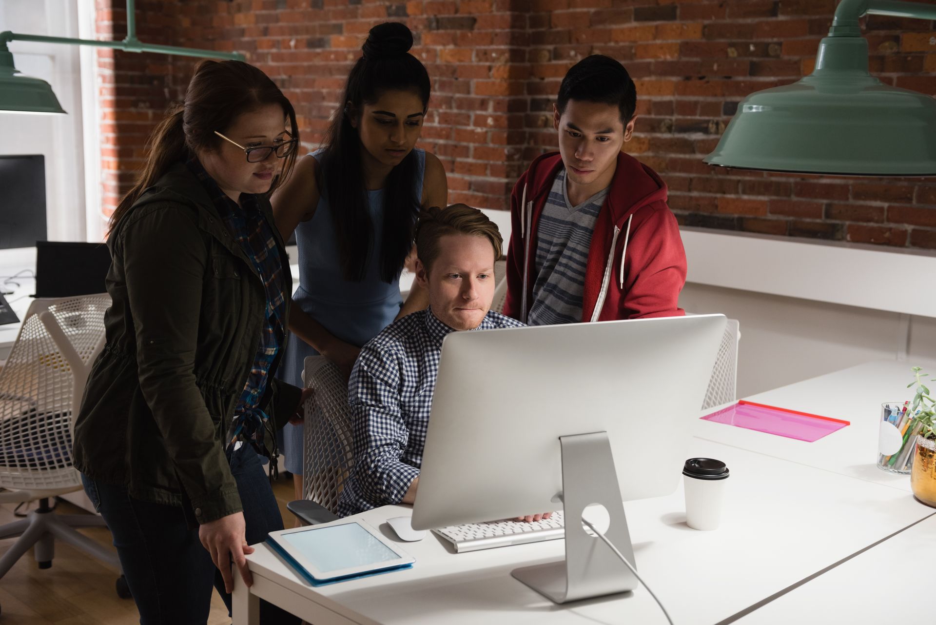 Four people collaborating around a computer in an office setting, looking at the screen.