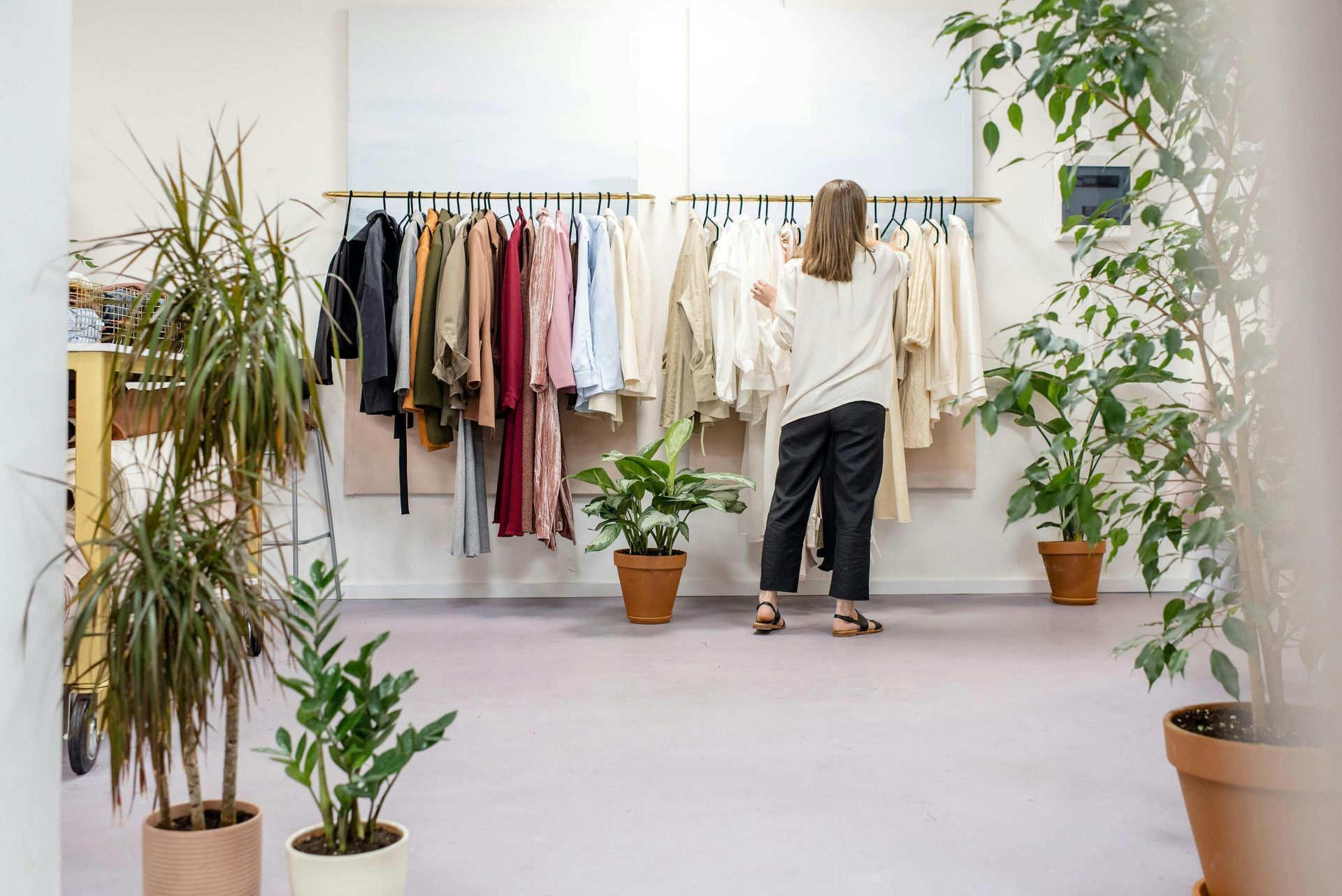 Woman browsing clothing rack in a boutique, surrounded by potted plants.