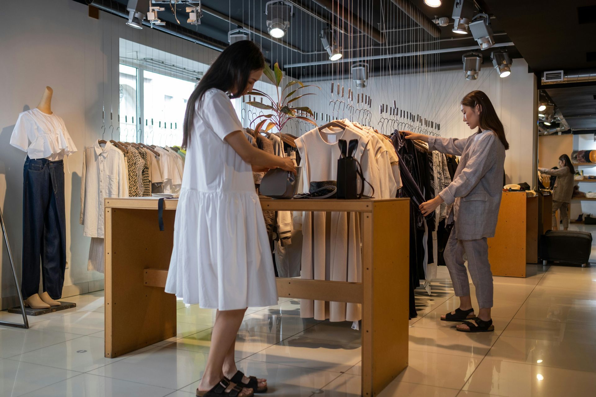 Two people browsing clothing in a brightly lit boutique, near racks and displays.