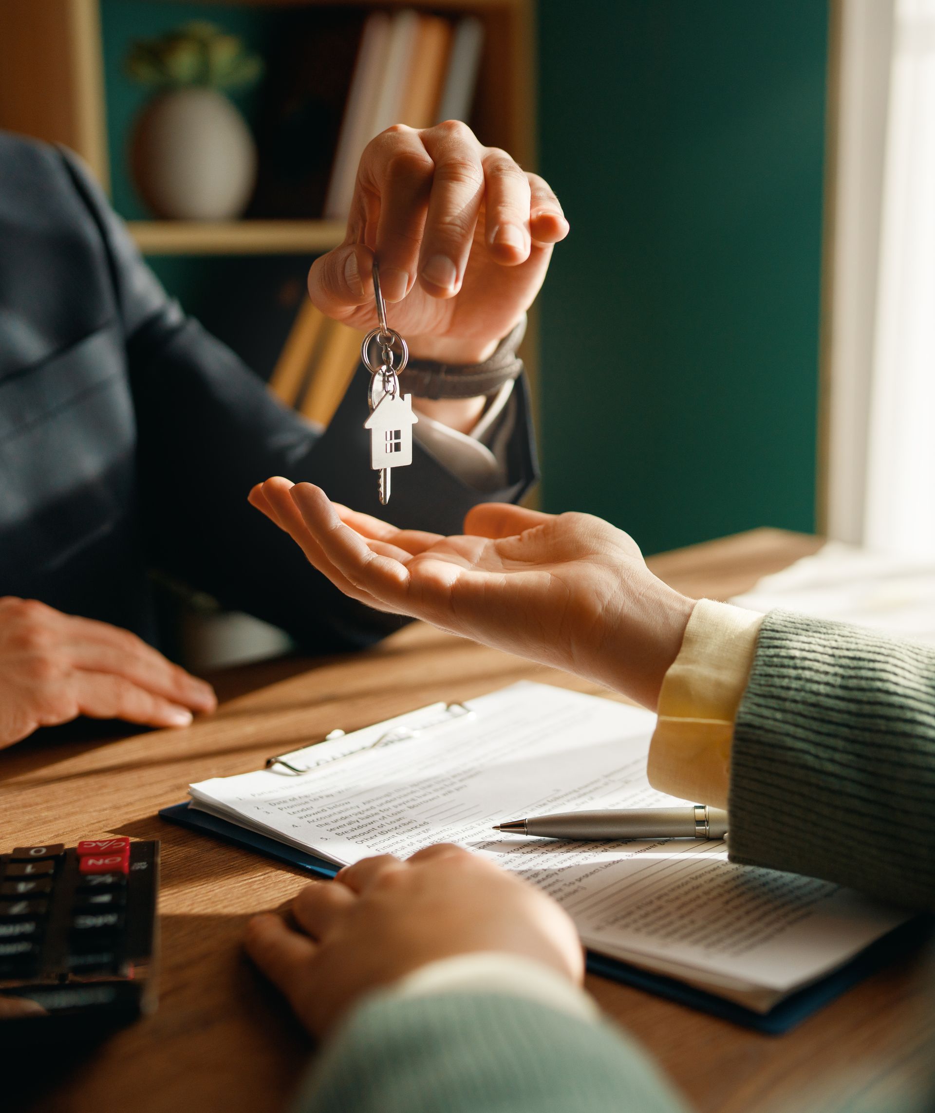 Person hands house keys to another over a document, likely a real estate transaction.