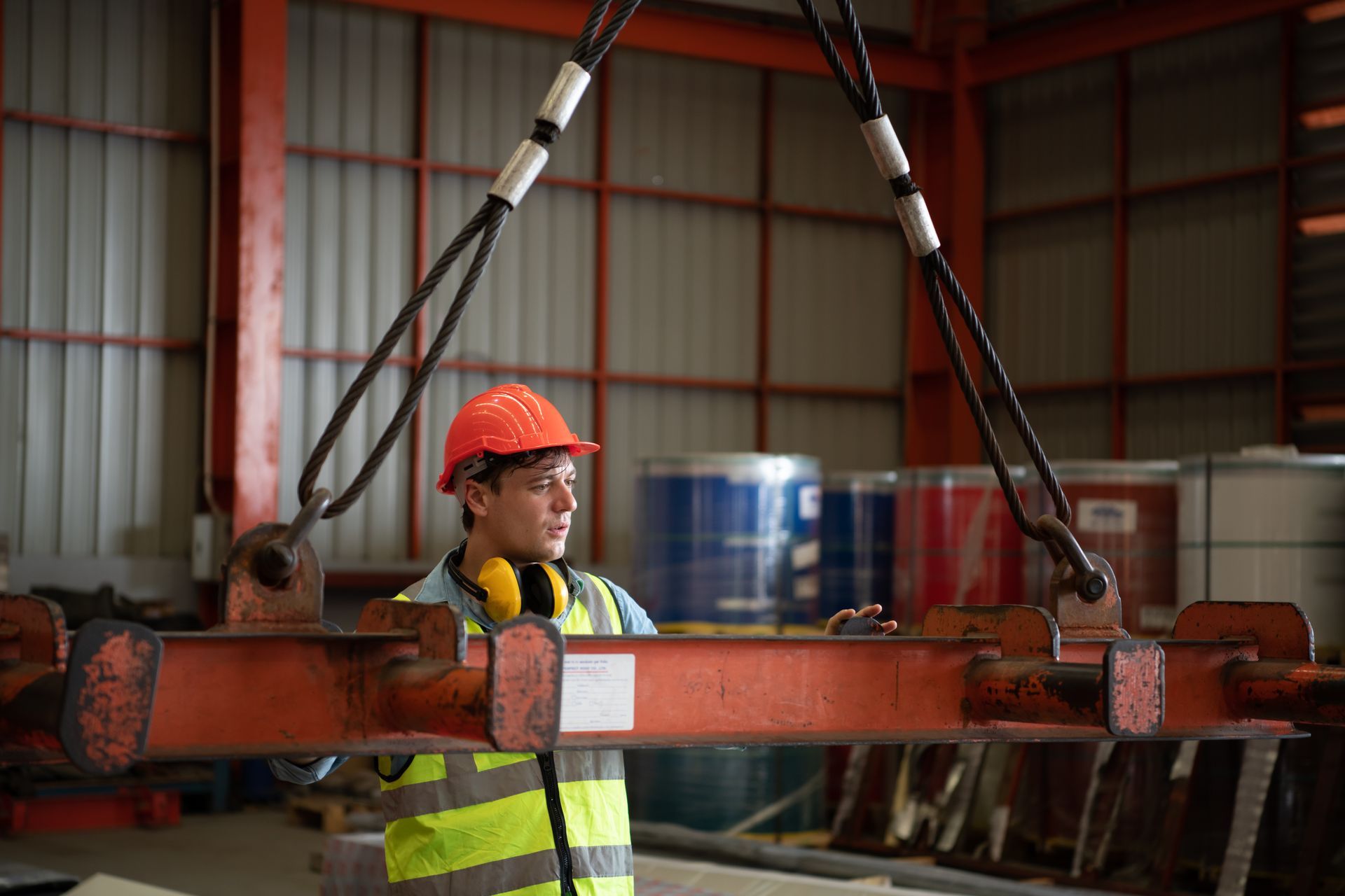 Construction worker in a warehouse inspecting a beam suspended by a crane.