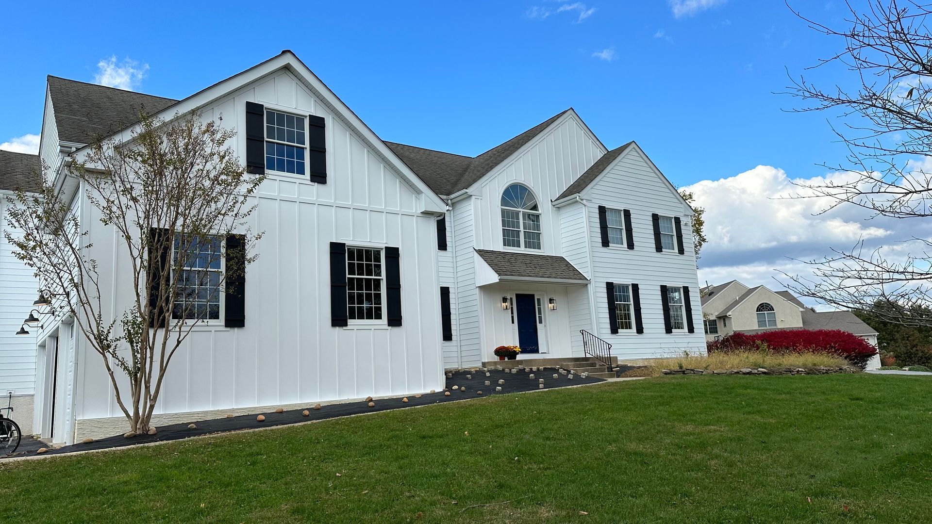 White house with black shutters, blue door, and green lawn under a blue sky.