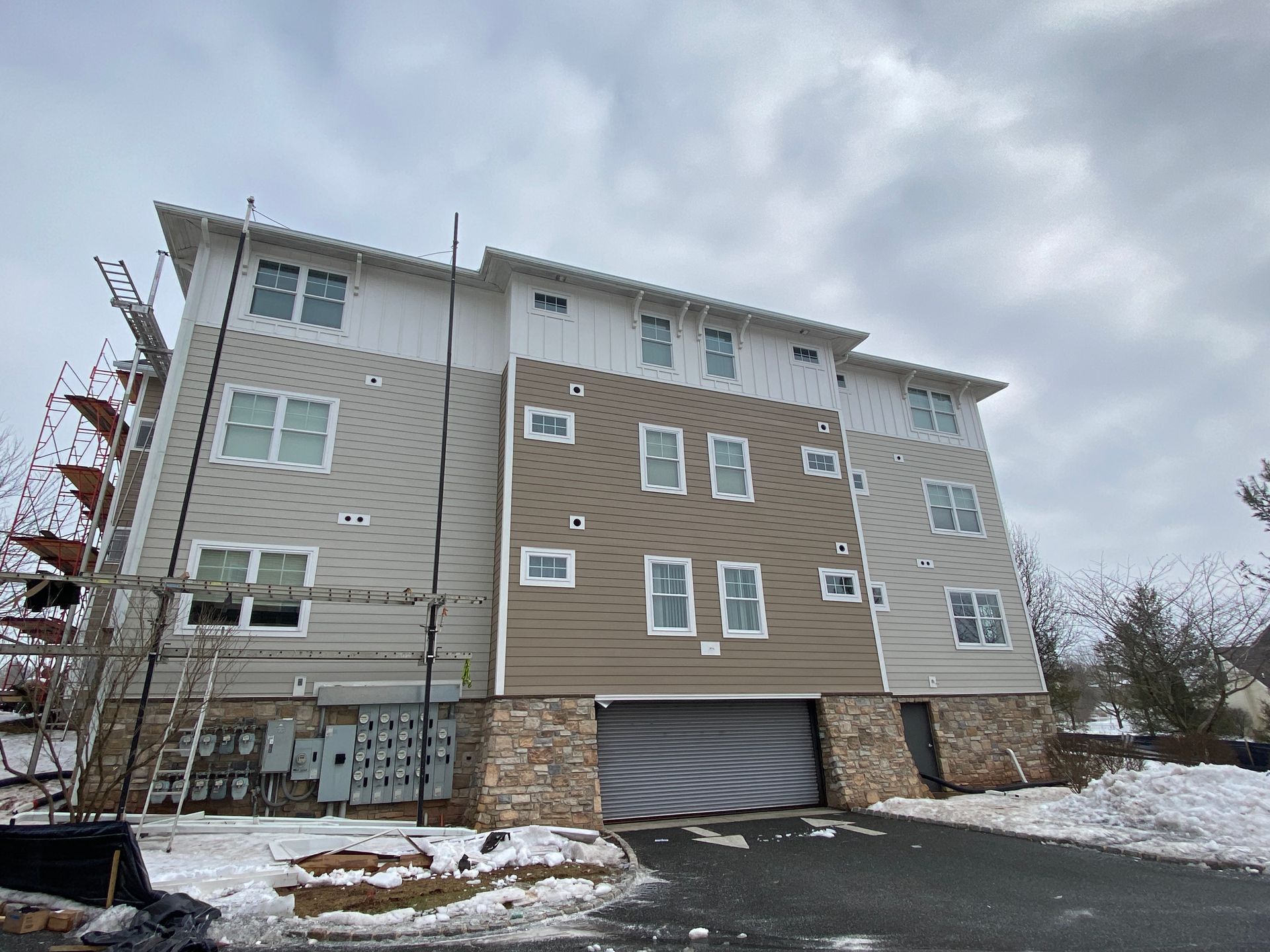 Multi-story building with white, tan, and brown siding; a garage; and snow-covered ground.