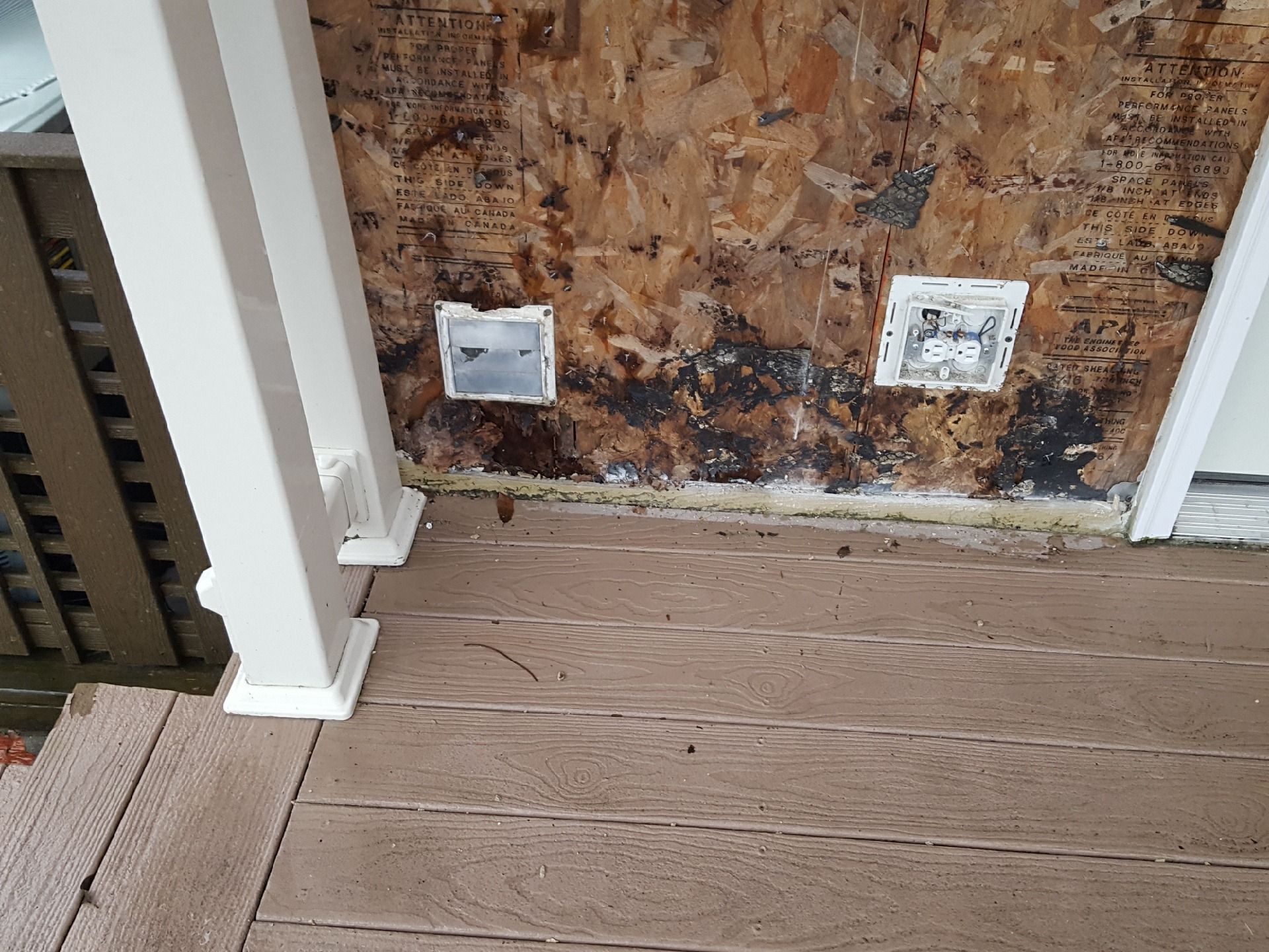 Damaged exterior wall with electrical outlets, mold, and composite decking.