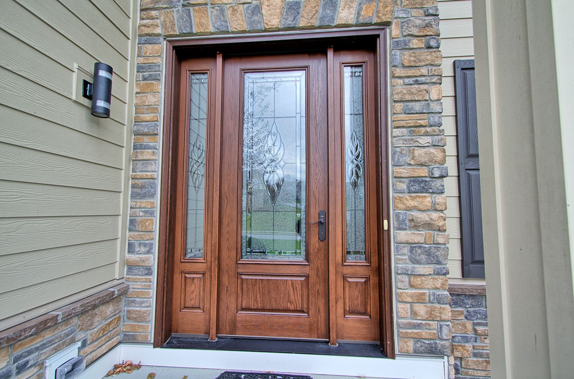 Wooden front door with glass panels framed by stone and siding.