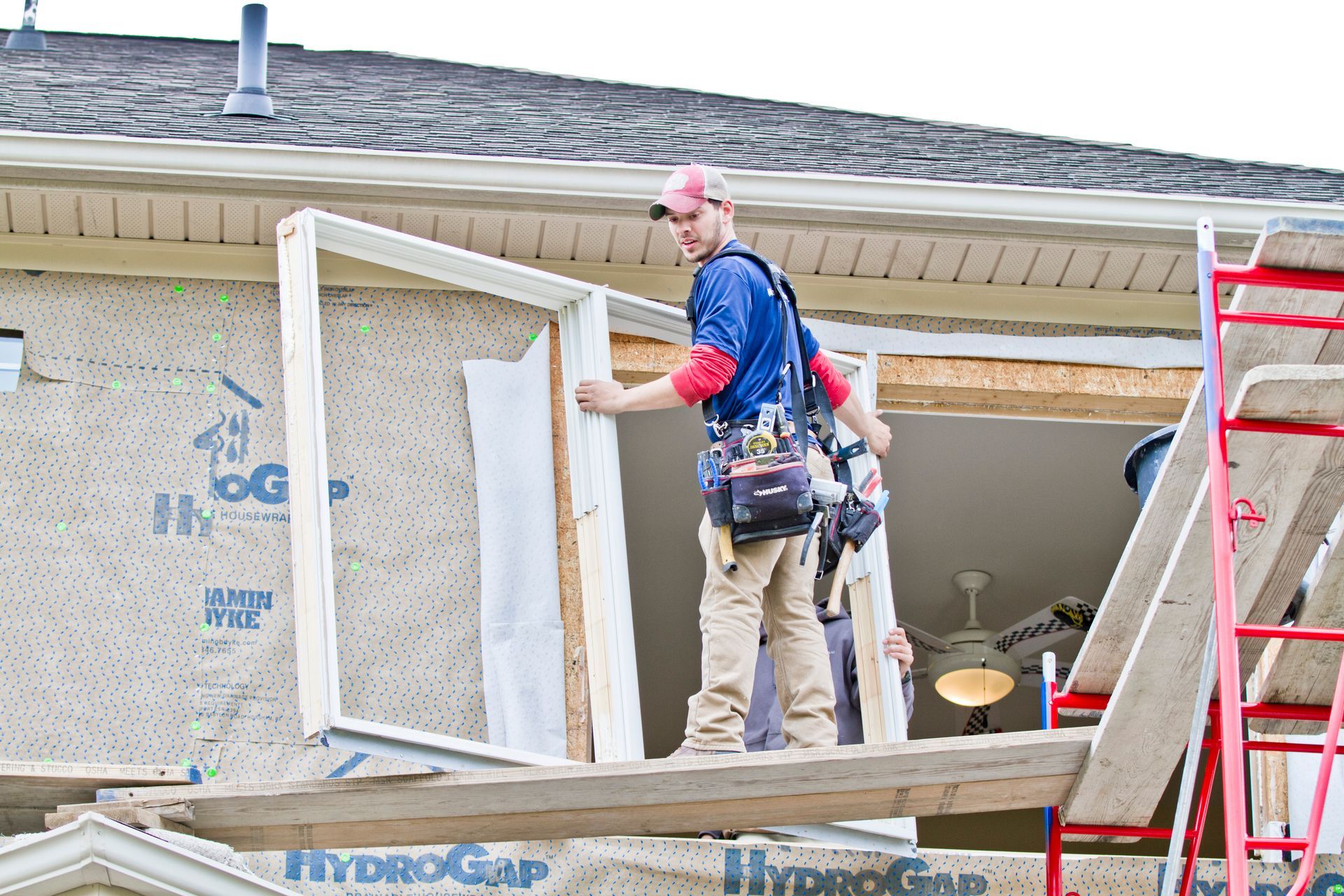 Construction worker installing window frame on scaffolding.
