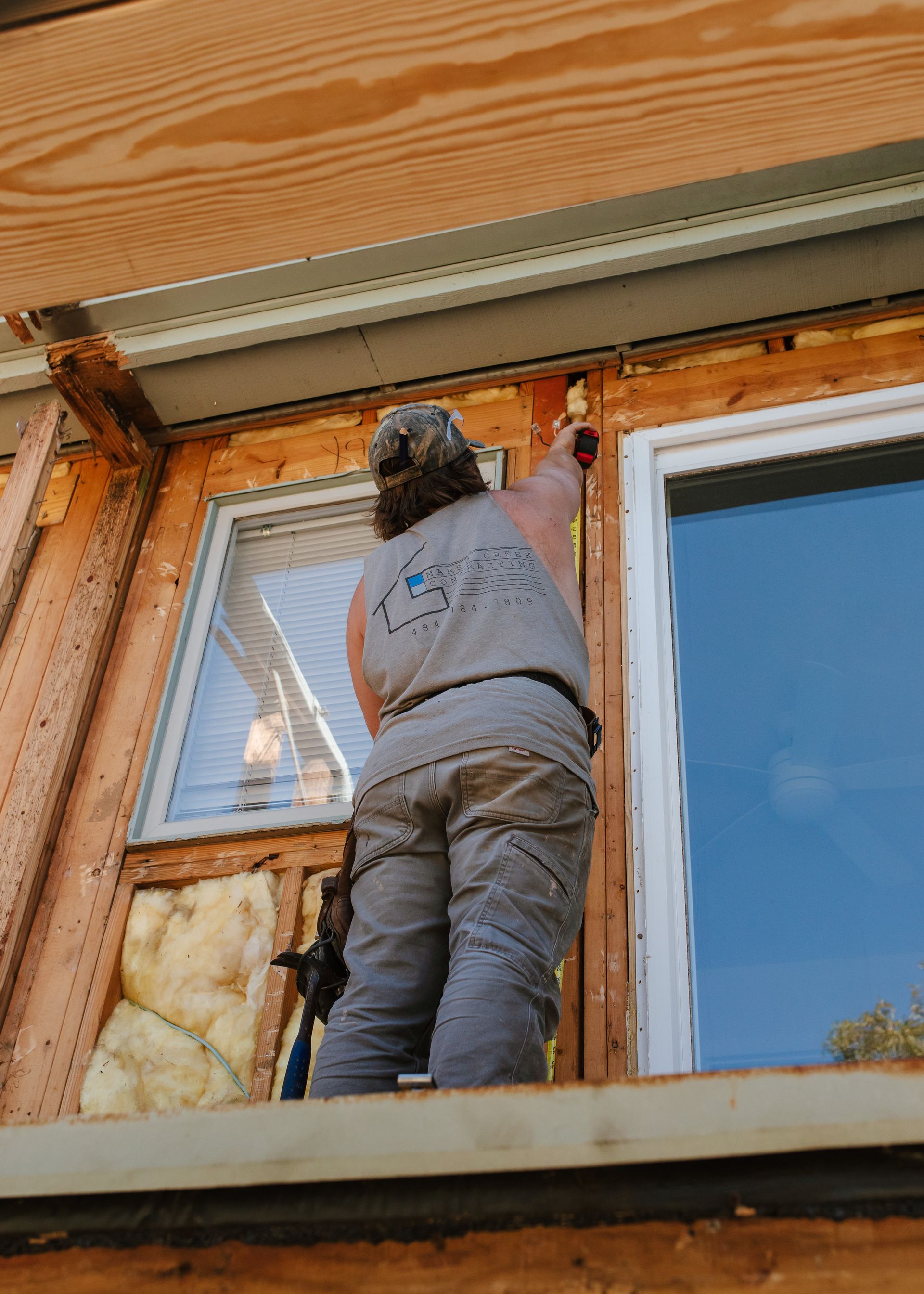 Person in work clothes caulking around a window frame on a building exterior.