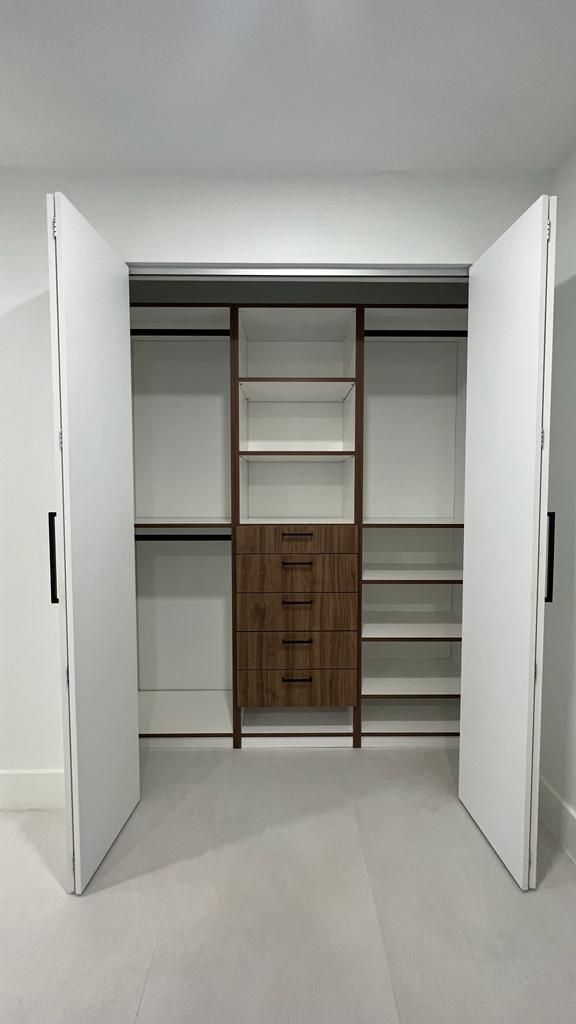 A walk in closet with the doors open and shelves and drawers.