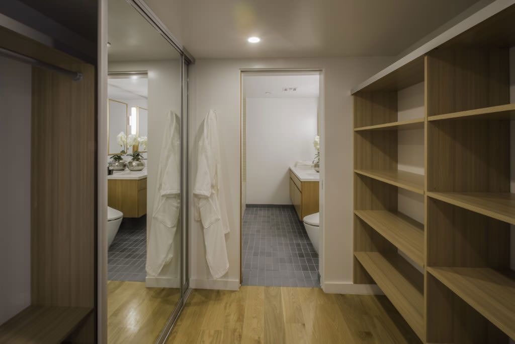 A walk in closet with a large mirror and wooden shelves leading to a bathroom.