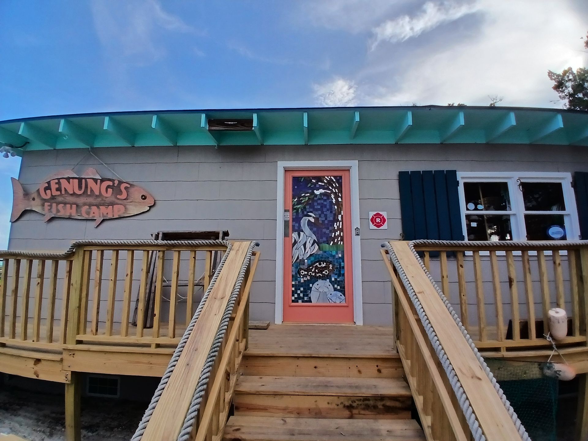 Small building with wooden ramp and stairs, teal roof trim, and colorful front door.