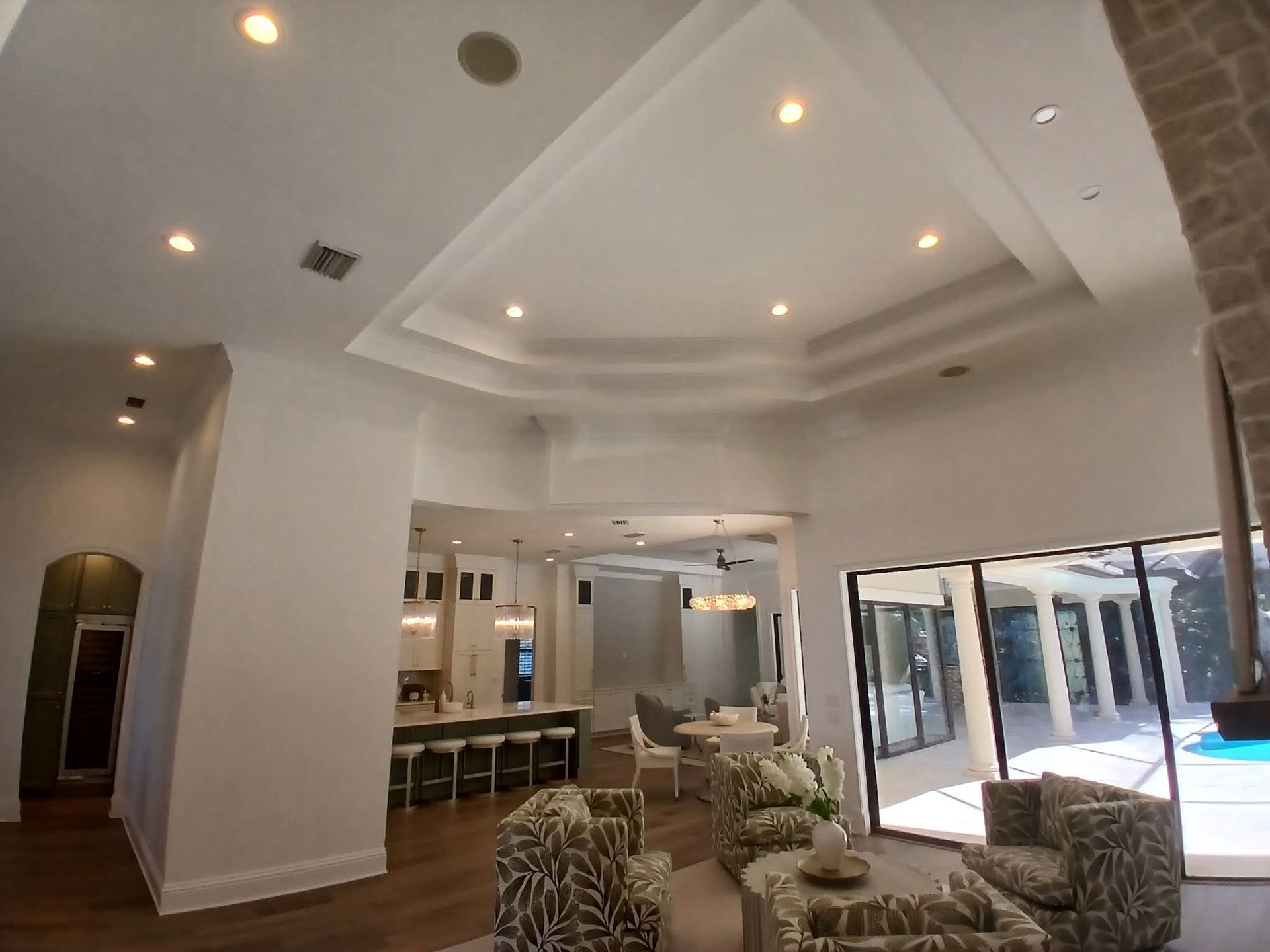 Bright hotel lobby with white ceiling lights, seating, and glass doors opening to a patio