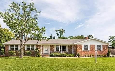 Single-story brick house with white trim and a large green lawn under a partly cloudy sky