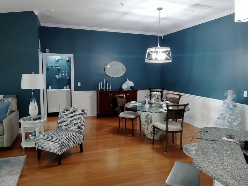 Modern dining room with blue walls, wooden floor, glass table, chairs, and patterned lounge chairs