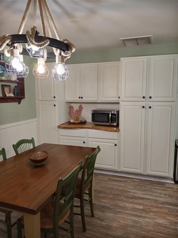 Dining room with white cabinets, wooden table and chairs, hanging light fixture, and microwave on the counter