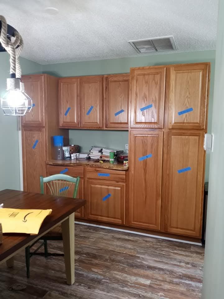 Small kitchen with wooden cabinets, cluttered countertop, dining table, and floor lamp on wood-look flooring