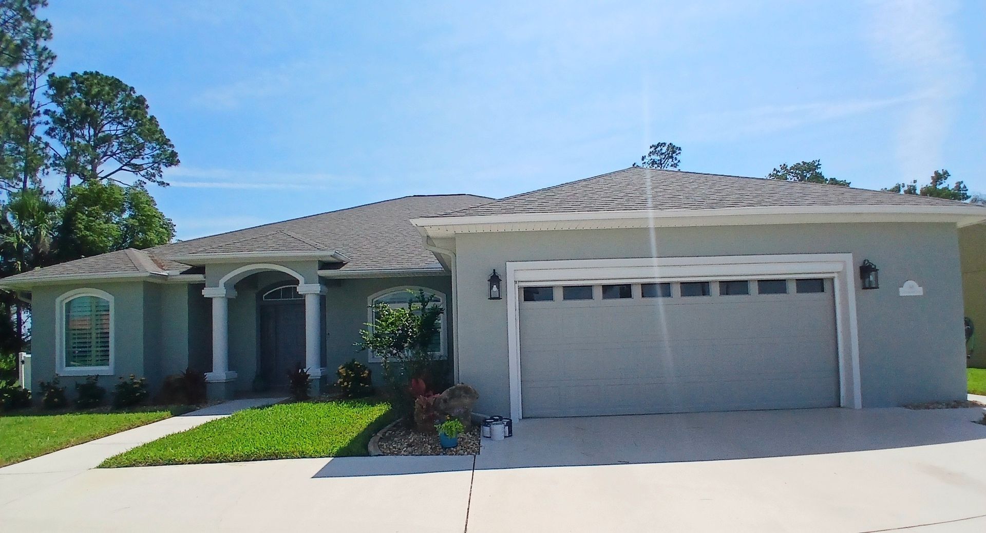 Light blue suburban house with a gray roof and attached garage on a sunny day.