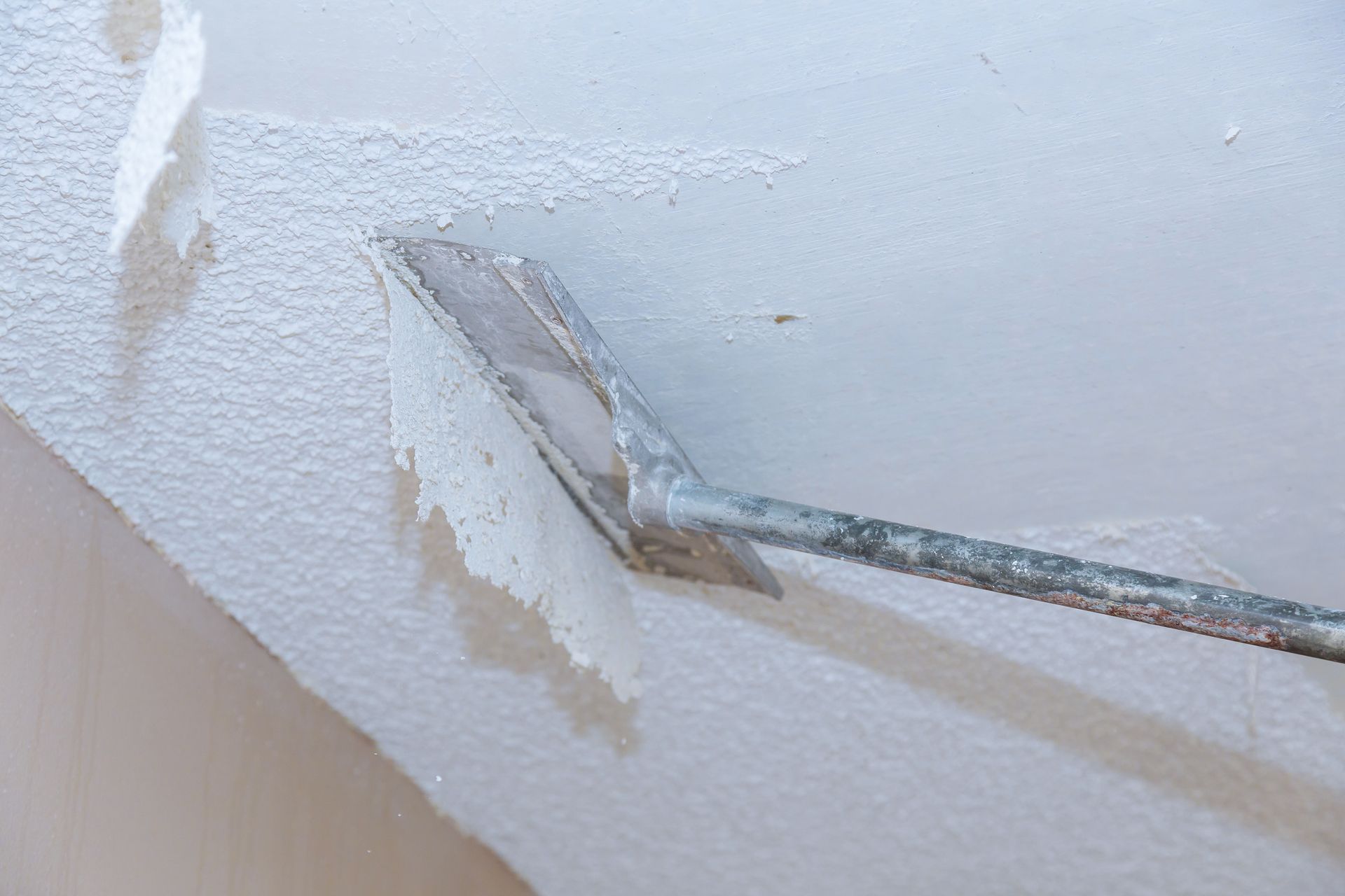 Ceiling being scraped with a drywall tool to remove peeling paint.