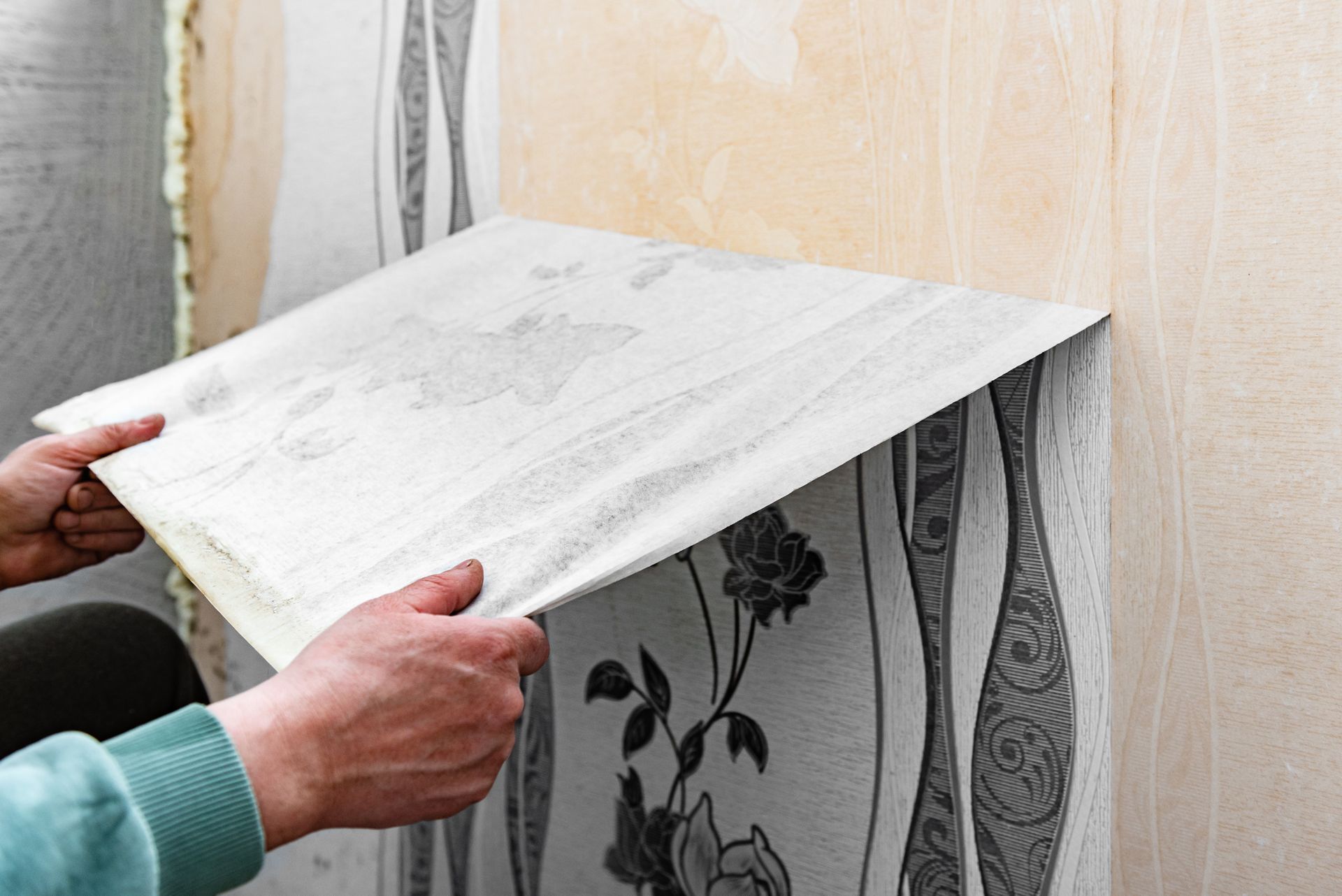 Person applying wallpaper to a wall, showing a floral pattern.