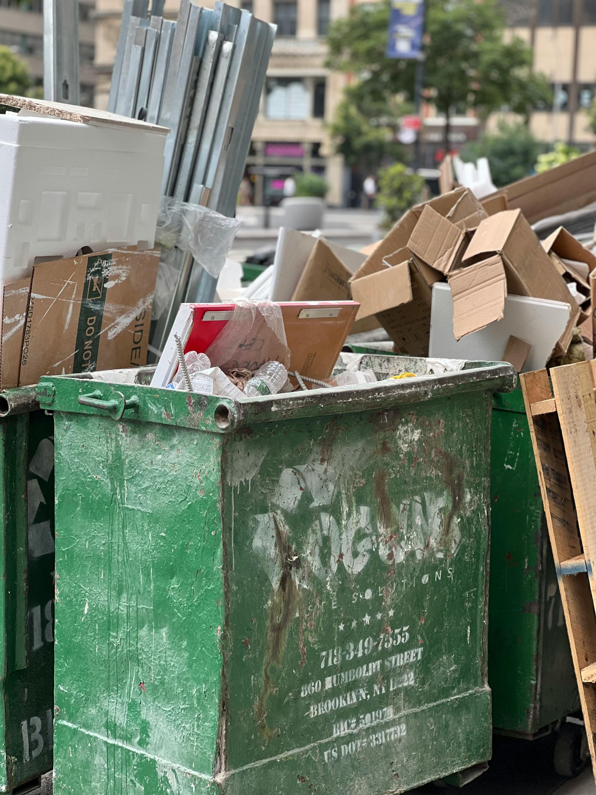 A green dumpster filled with cardboard boxes and wooden pallets.