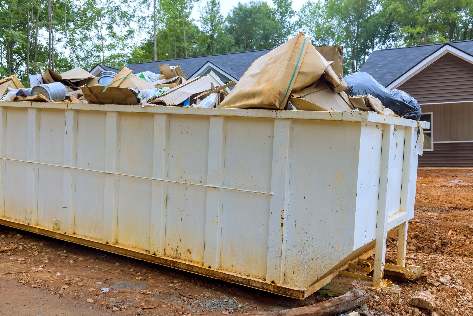 A large white dumpster filled with garbage is sitting in front of a house.