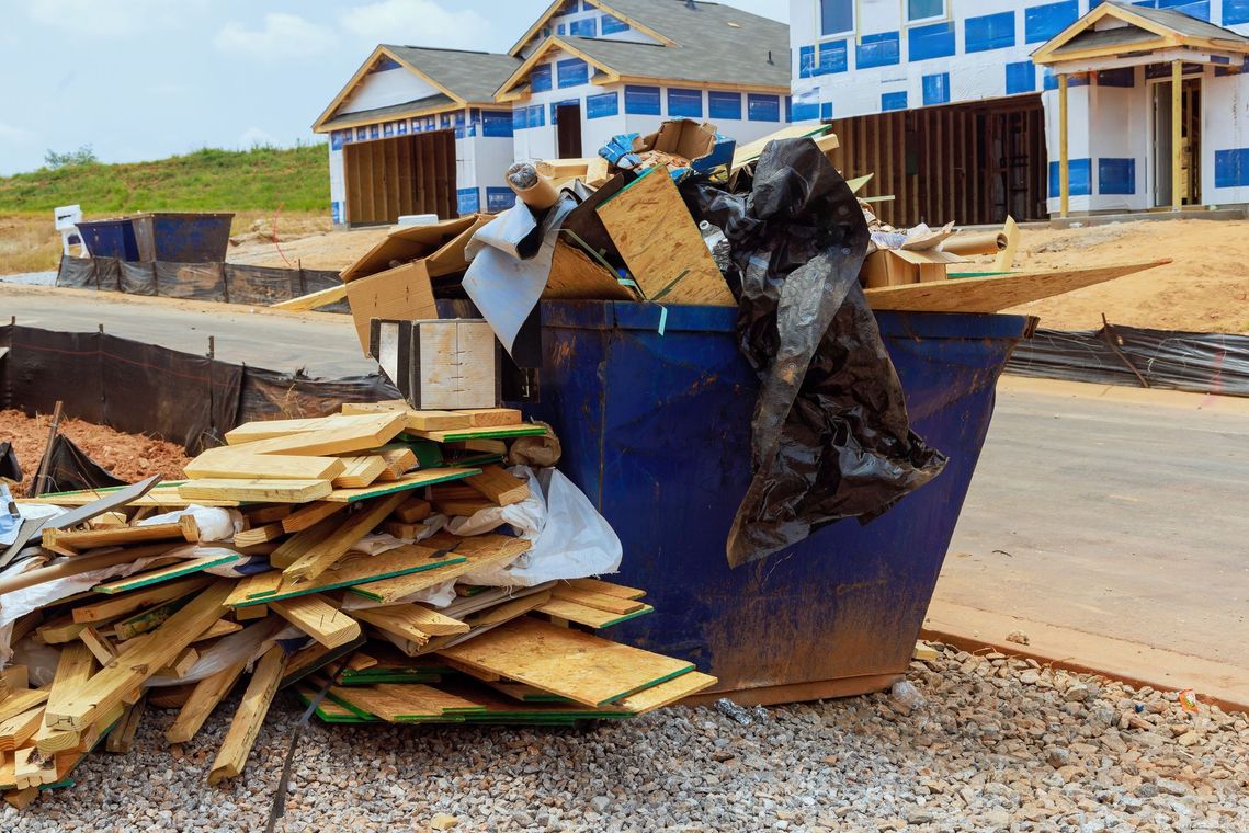 A dumpster filled with wood is sitting in front of a house under construction.