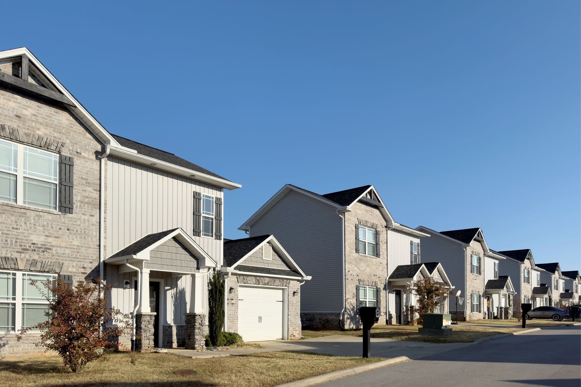 Row of modern townhouses with light-colored siding, gray brick accents, and clear blue sky.