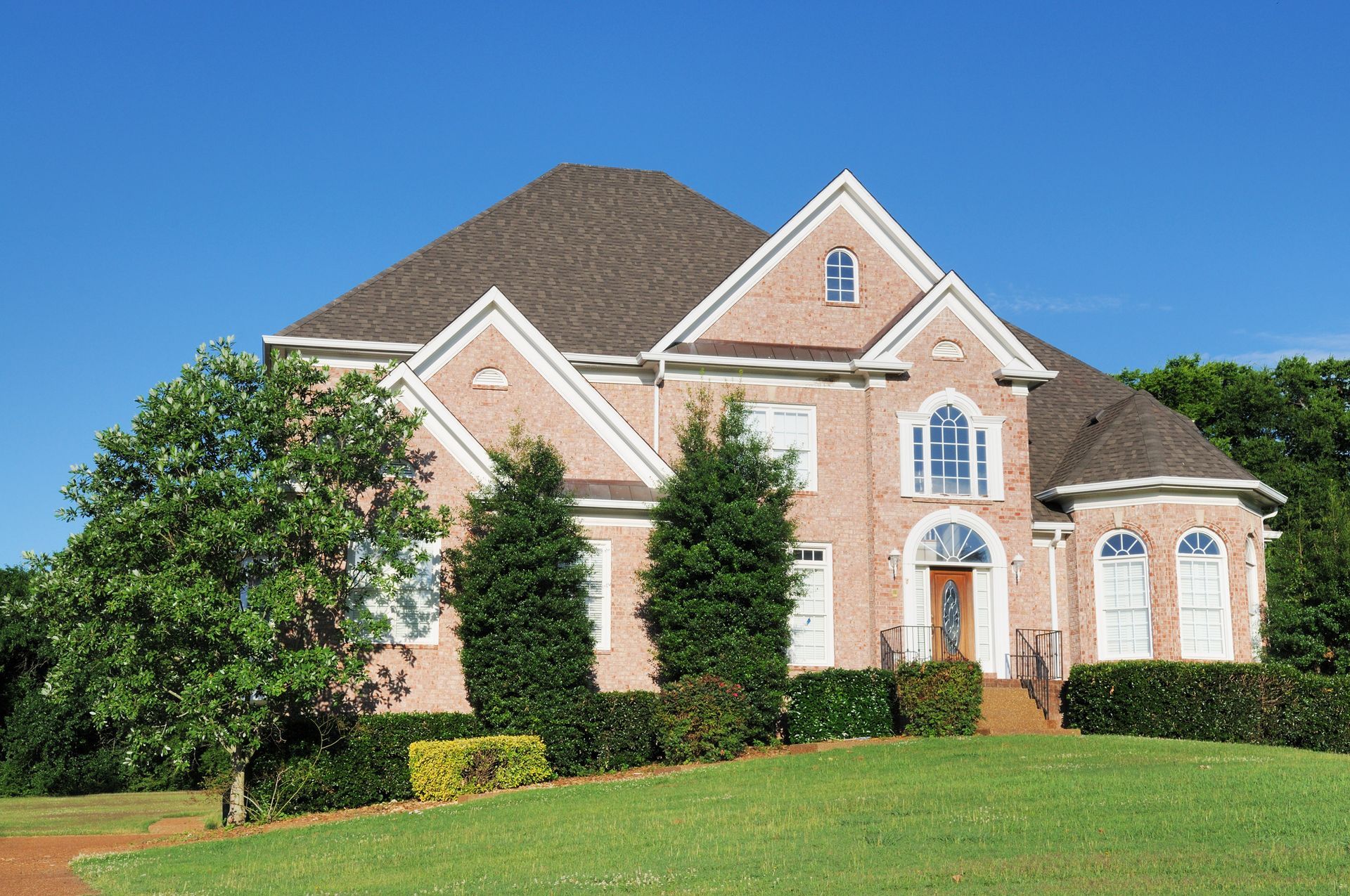 Two-story brick house with a brown roof and a green lawn under a clear blue sky.