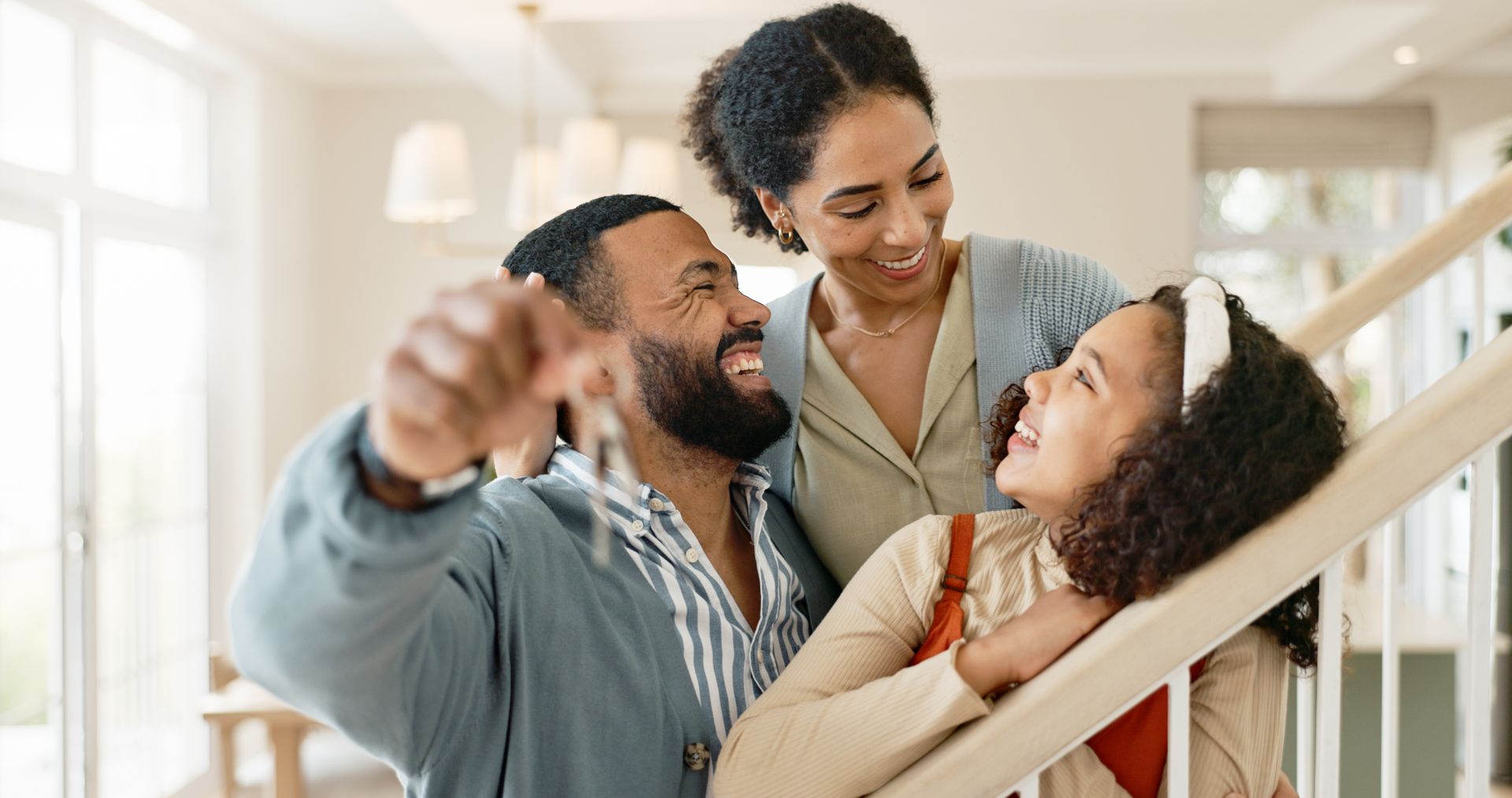 Family, smiling, with keys in hand, by a staircase.