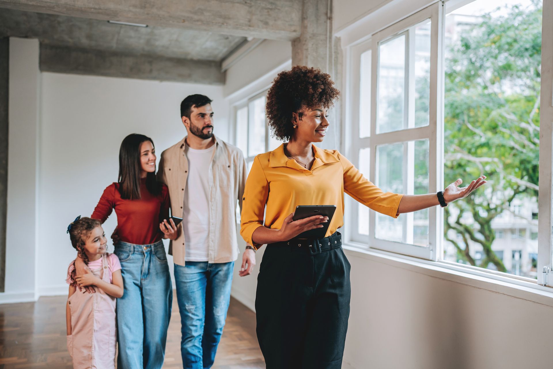 Real estate agent showing a home to a family; interior hallway with large windows.