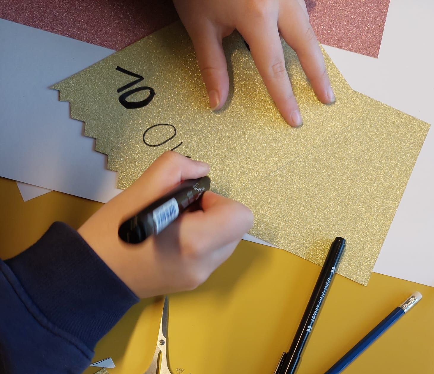 Meid schrijft met stift op glitterpapier als onderdeel van het ontwerpen van een poster.