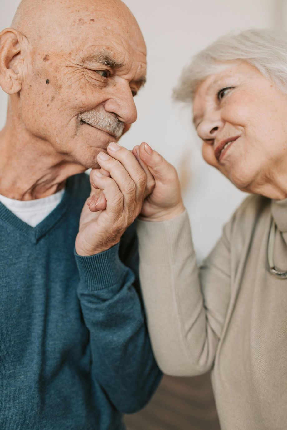 Elderly couple, holding hands, looking at each other lovingly. Man in blue sweater, woman in beige.