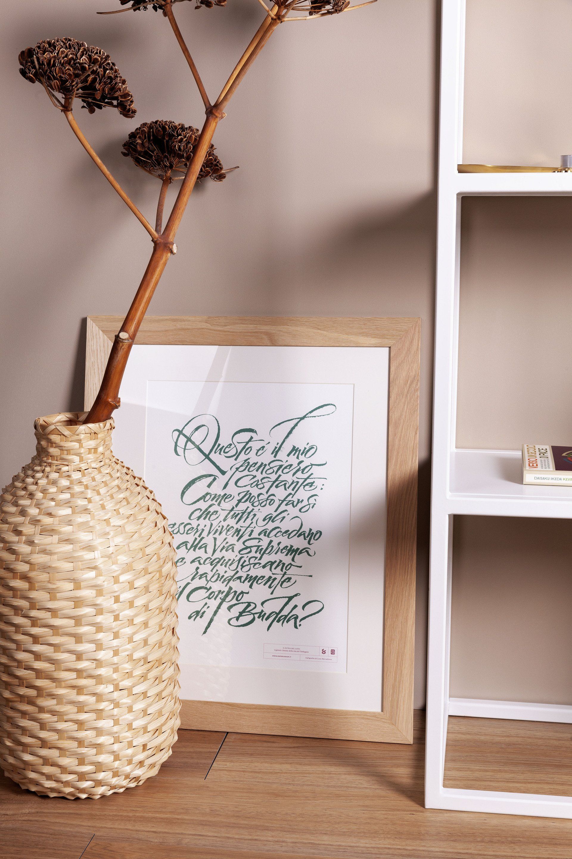 Un vaso di vimini è appoggiato accanto a una foto incorniciata su uno scaffale.