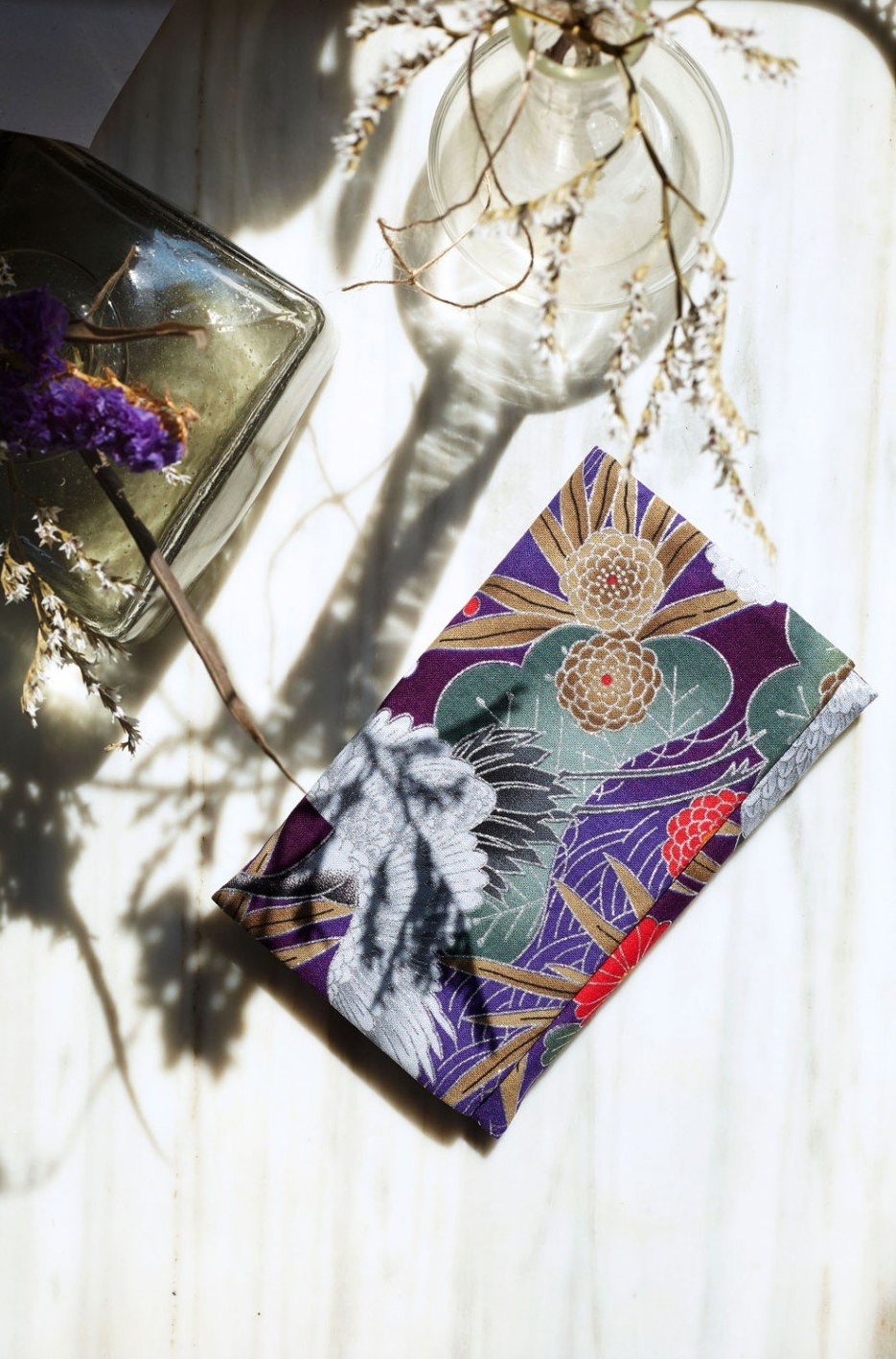 Un tovagliolo viola è appoggiato su un tavolo accanto a un vaso di fiori.