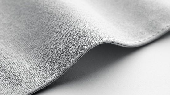 Primer plano de una tela gris claro con superficie texturizada y borde ligeramente curvado sobre un fondo blanco.