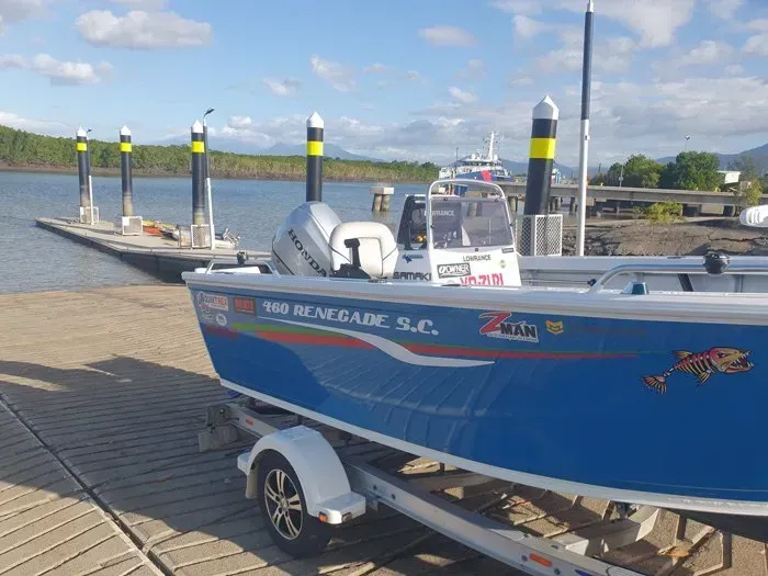Blue and White Fishing Boat on A Trailer Parked at A Dock with Pylons, Sky, and Trees in The Background — HiTune Marine In Bentley Park, QLD