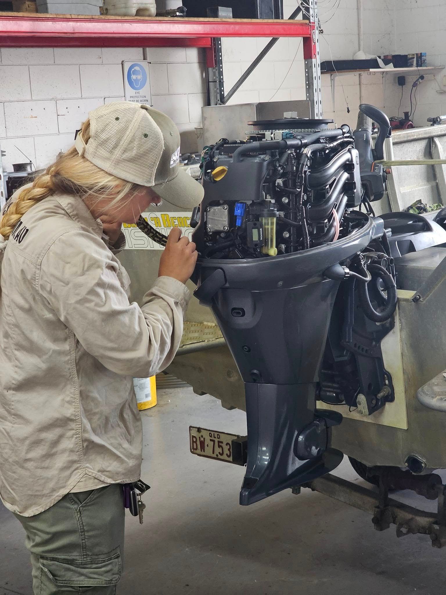 A Person in Tan Workwear Examines a Boat Motor Attached to A Boat in A Repair Shop — HiTune Marine In Mossman, QLD 