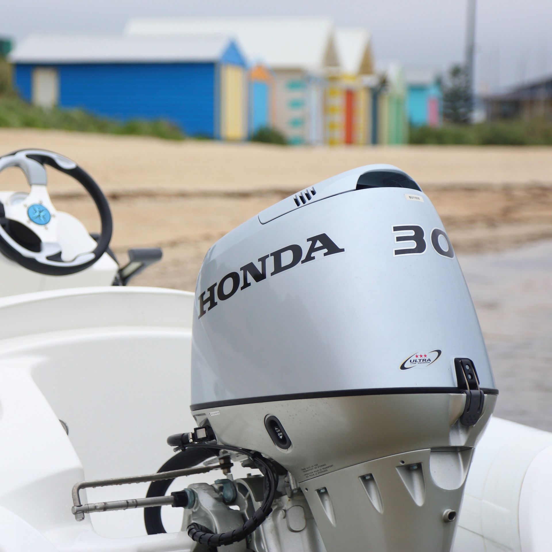 Honda 30 Outboard Motor on A White Boat at A Beach with Colorful Huts in The Background — HiTune Marine In Mareeba, QLD